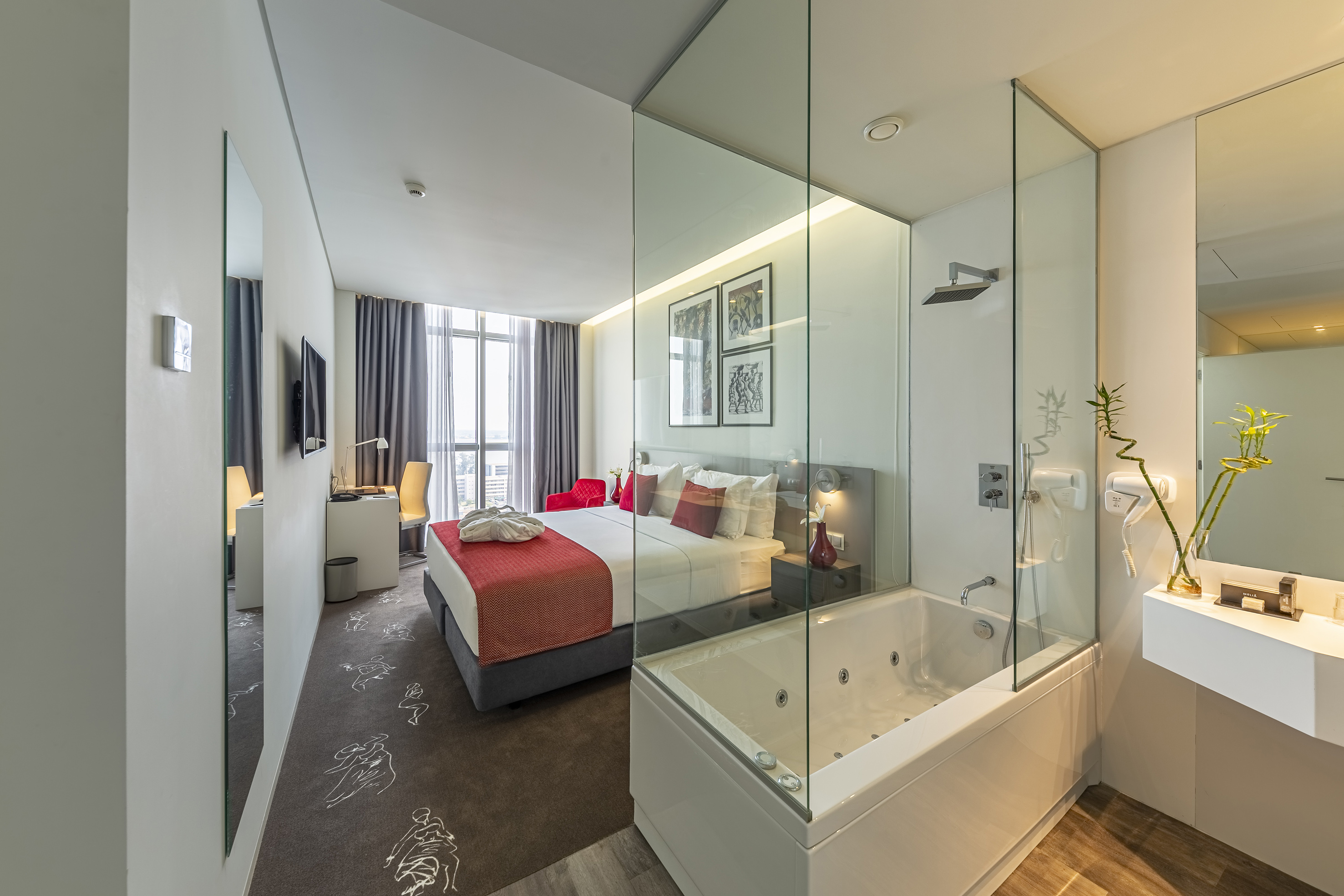 Modern hotel room with bed, glass-walled jacuzzi, and city view.
