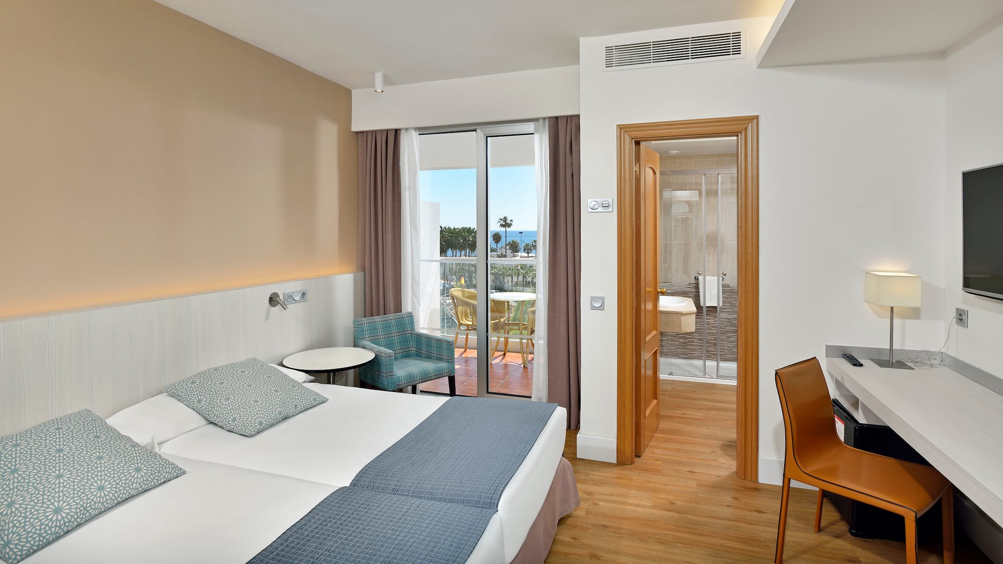 Hotel room with twin beds, sea view balcony, desk, and open bathroom.