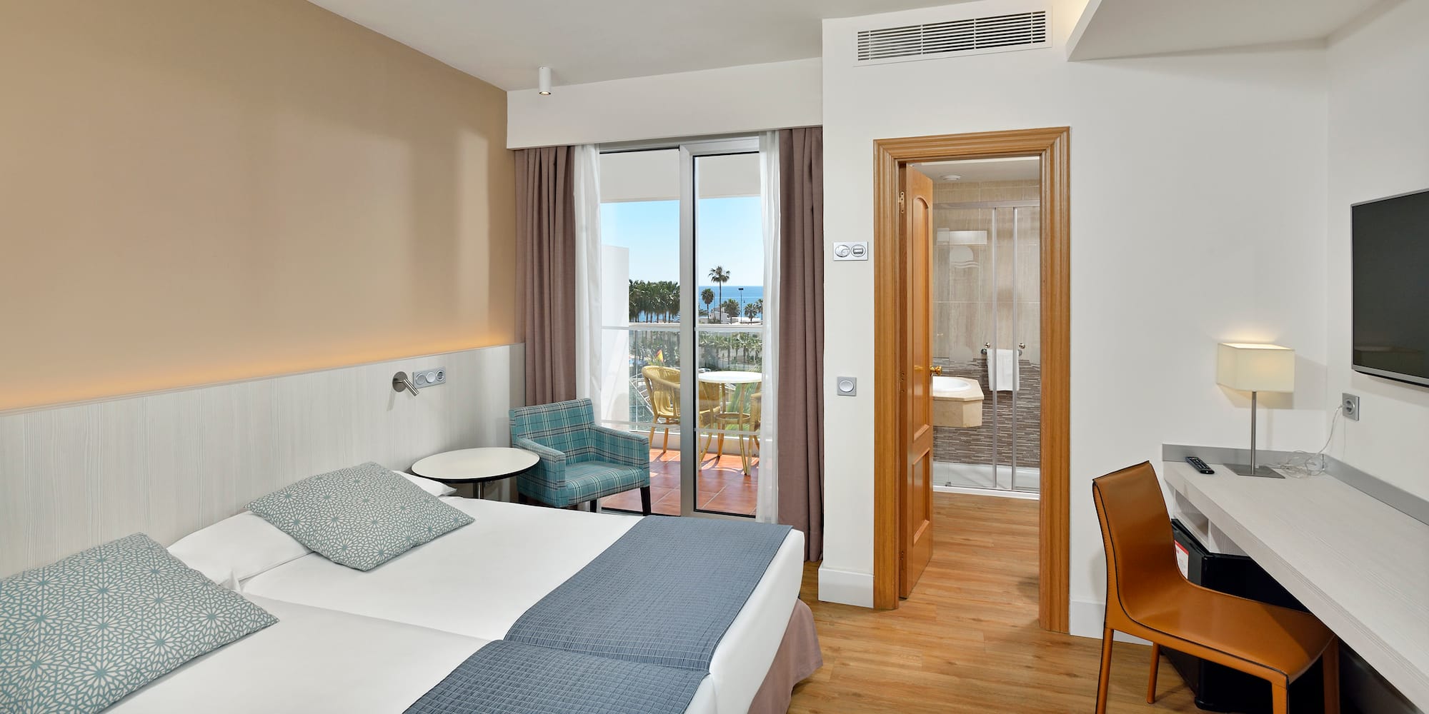 Hotel room with twin beds, sea view balcony, desk, and open bathroom.