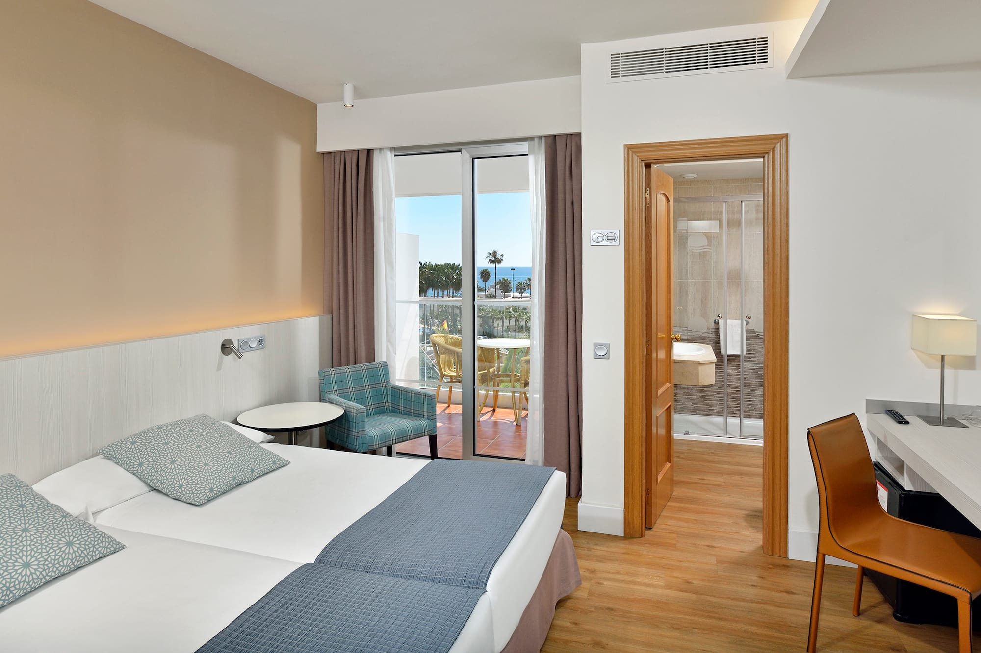 Hotel room with twin beds, sea view balcony, desk, and open bathroom.