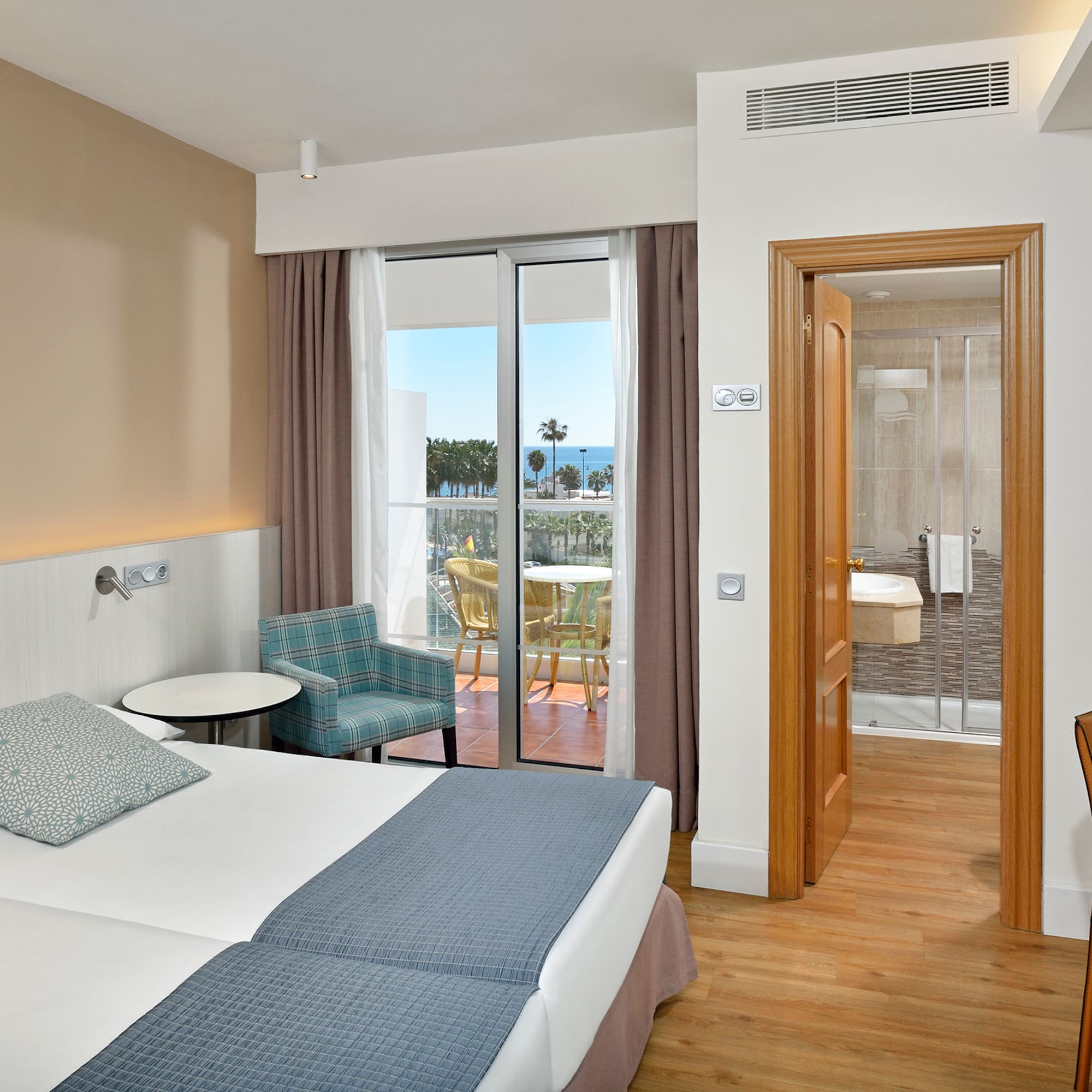 Hotel room with twin beds, sea view balcony, desk, and open bathroom.