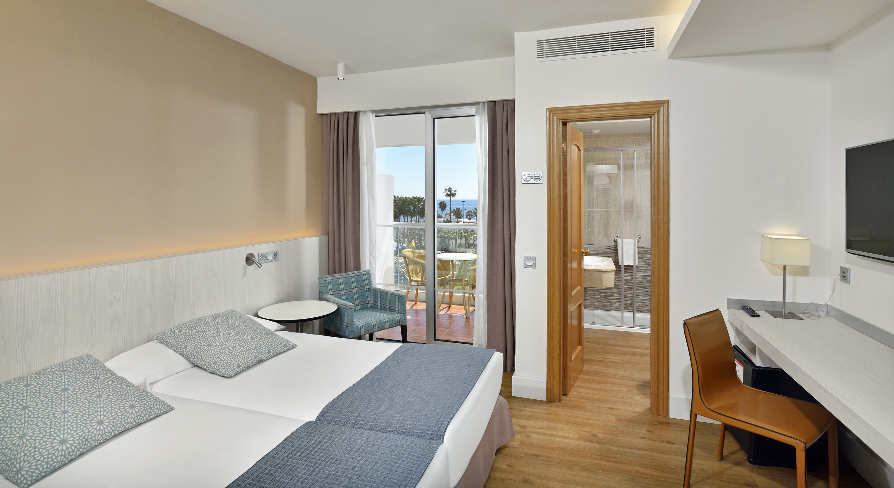 Hotel room with twin beds, sea view balcony, desk, and open bathroom.
