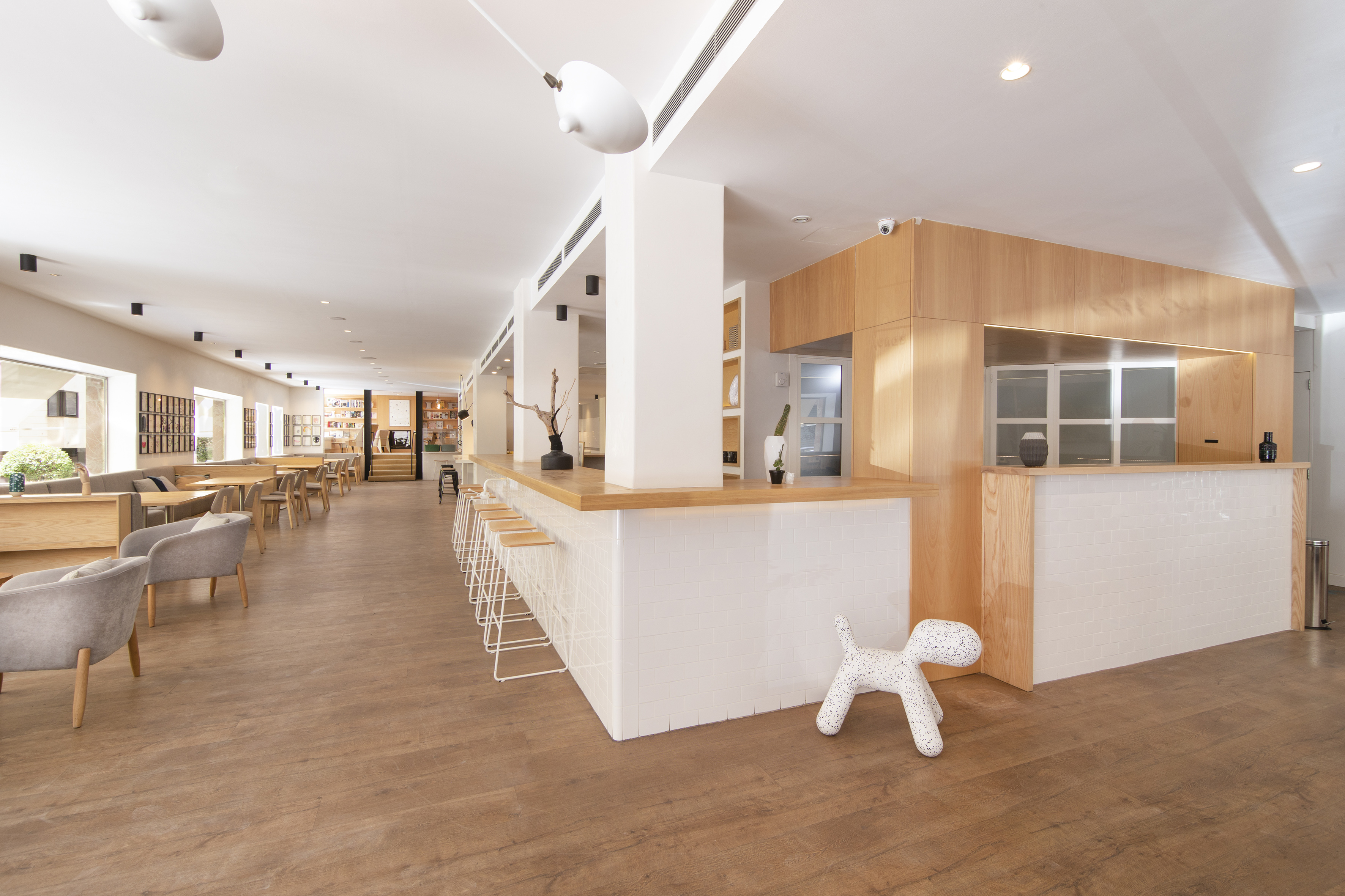 Modern cafe interior with white bar, wooden floors, and ample lounge seating.