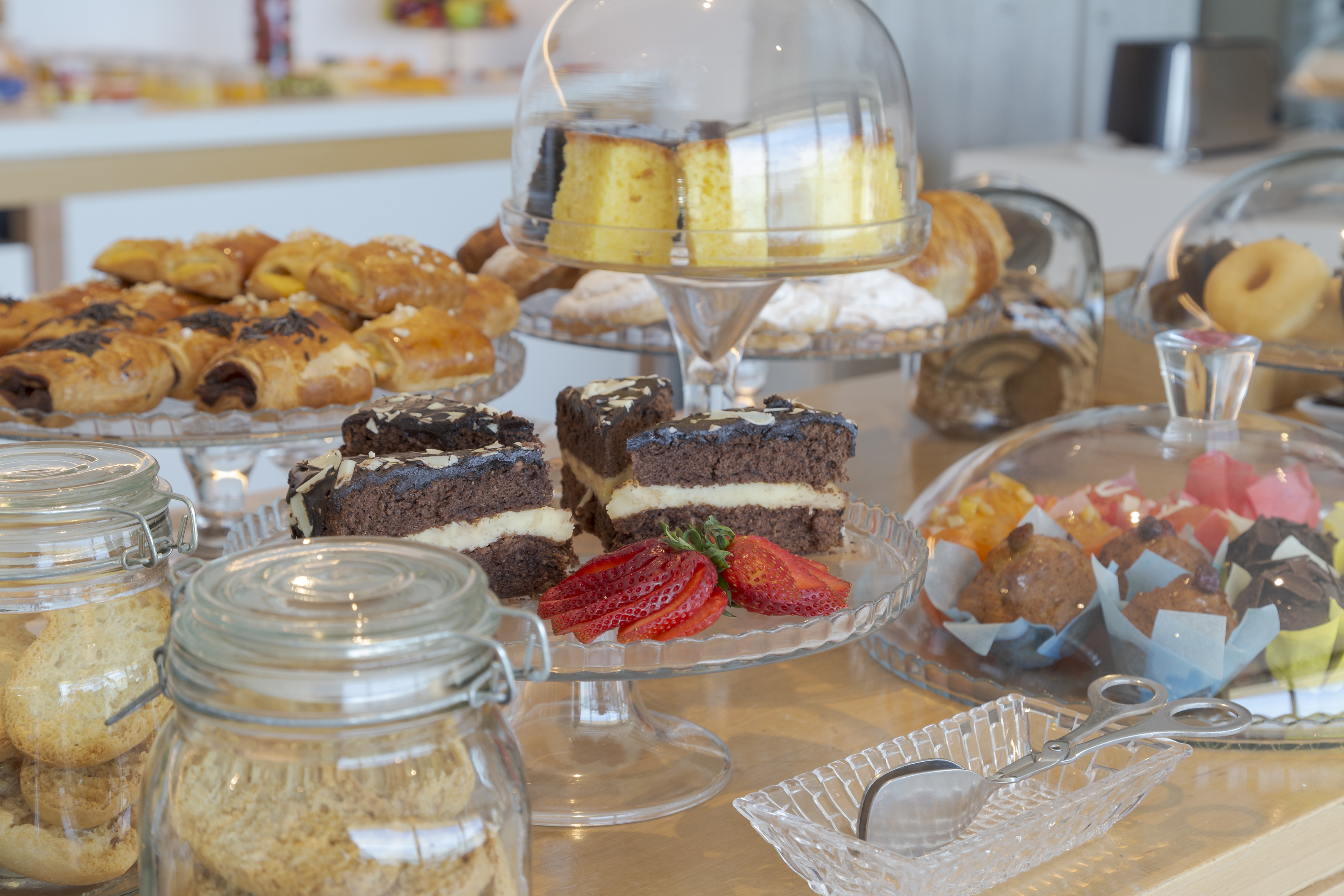 Assorted breakfast buffet featuring cakes, pastries, muffins, and jars of cookies.