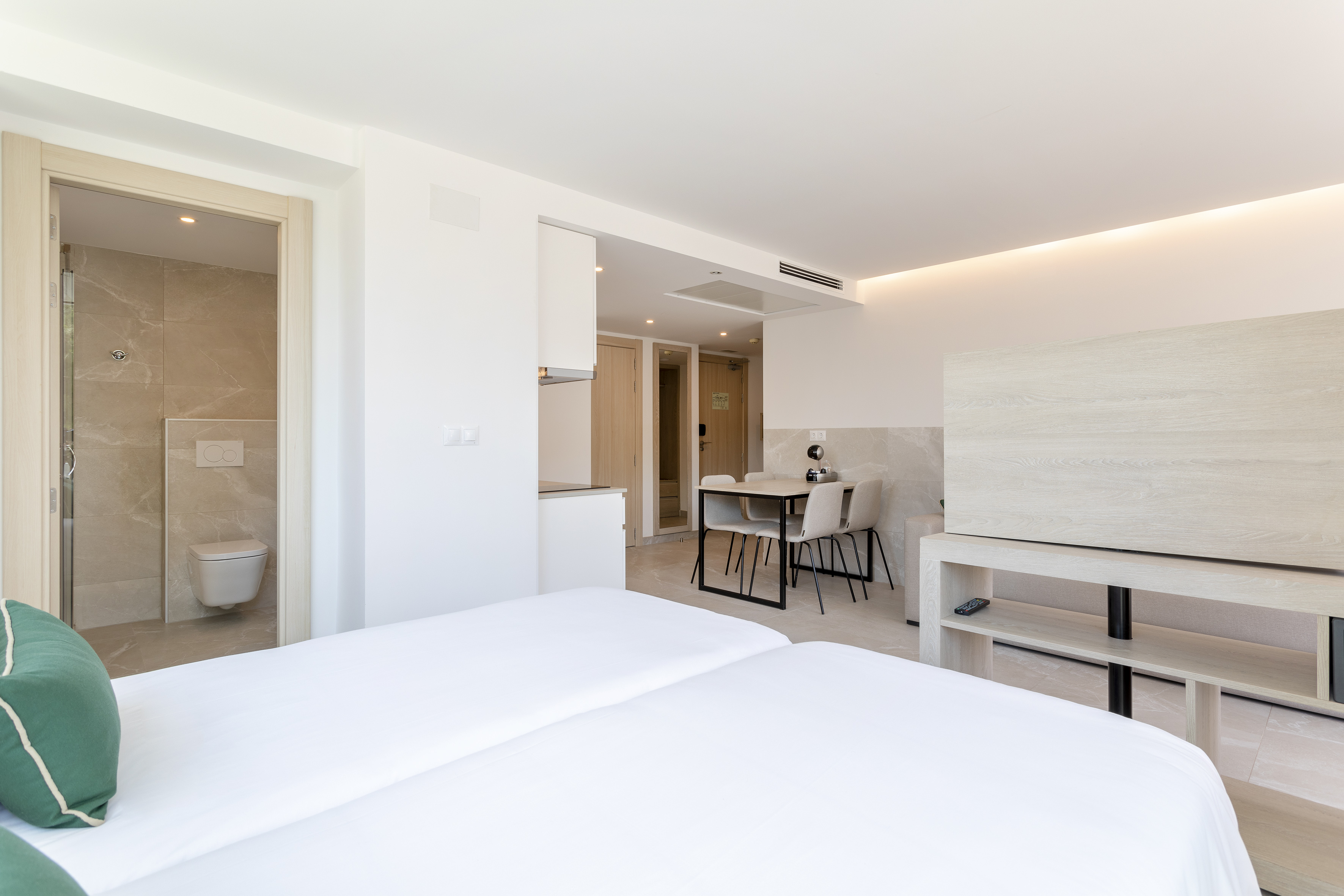 Bright hotel studio with twin beds, private bathroom, and dining table.