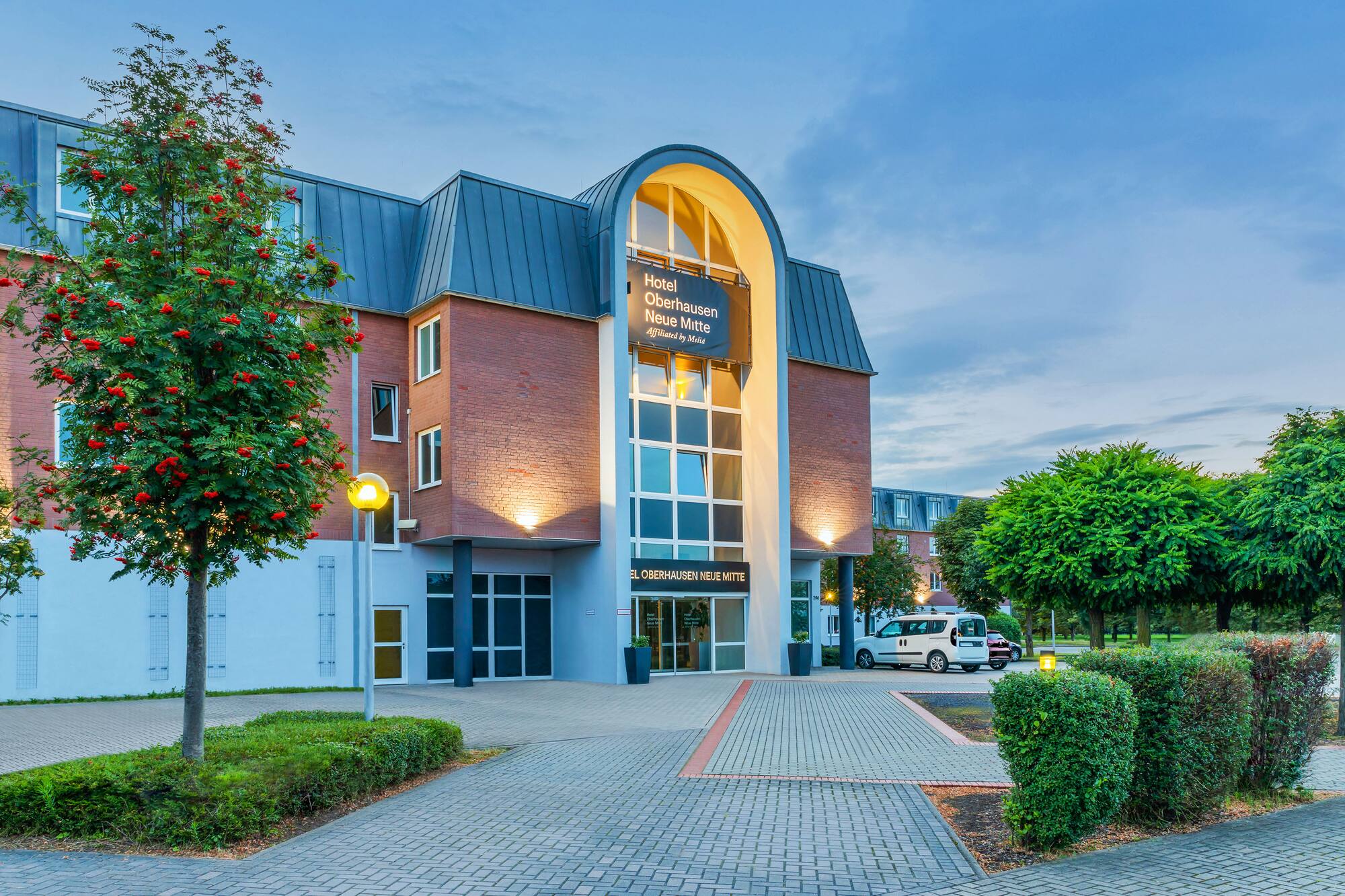 Hotel Oberhausen Neue Mitte, modern building with arched glass entrance and tree.