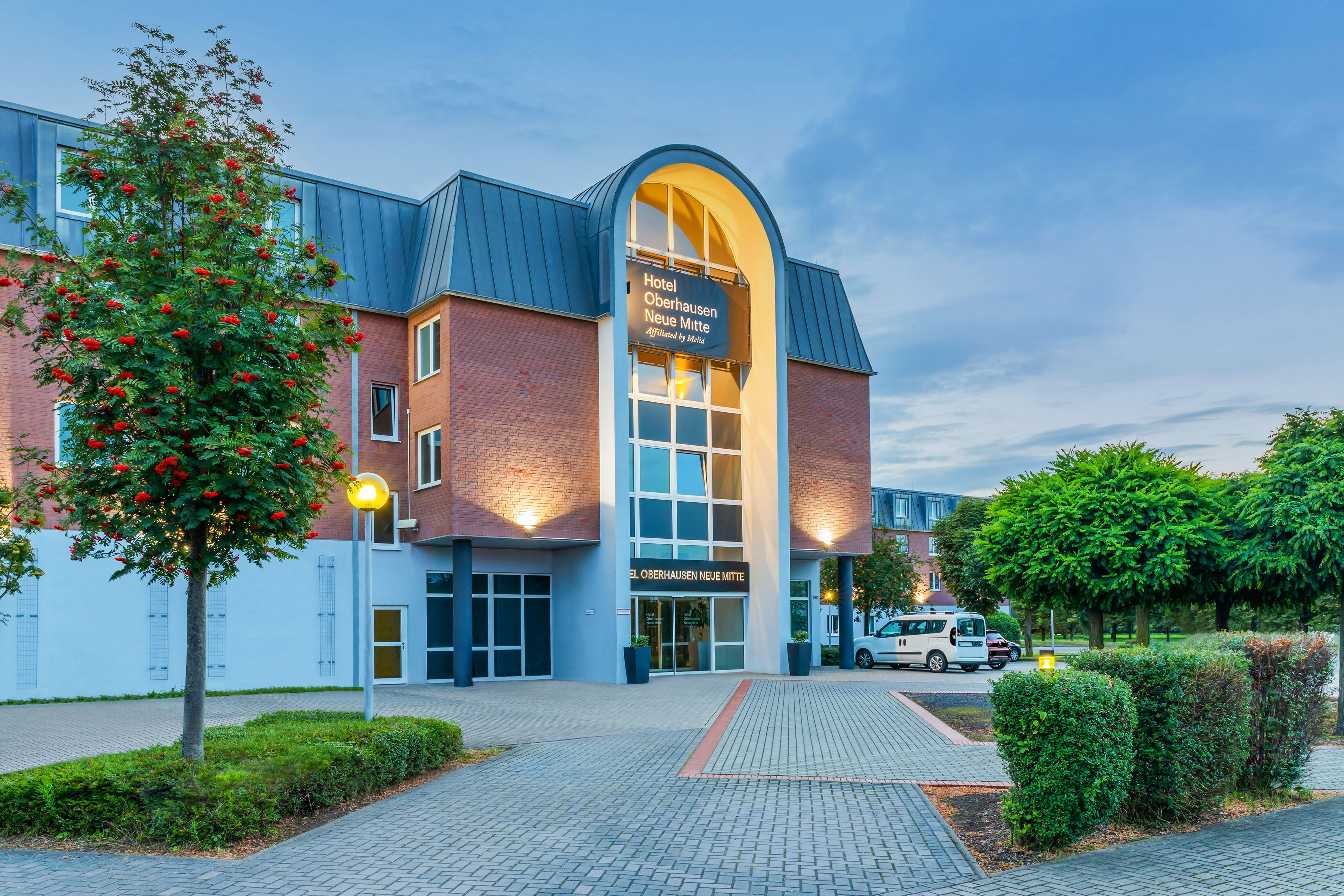 Hotel Oberhausen Neue Mitte, modern building with arched glass entrance and tree.