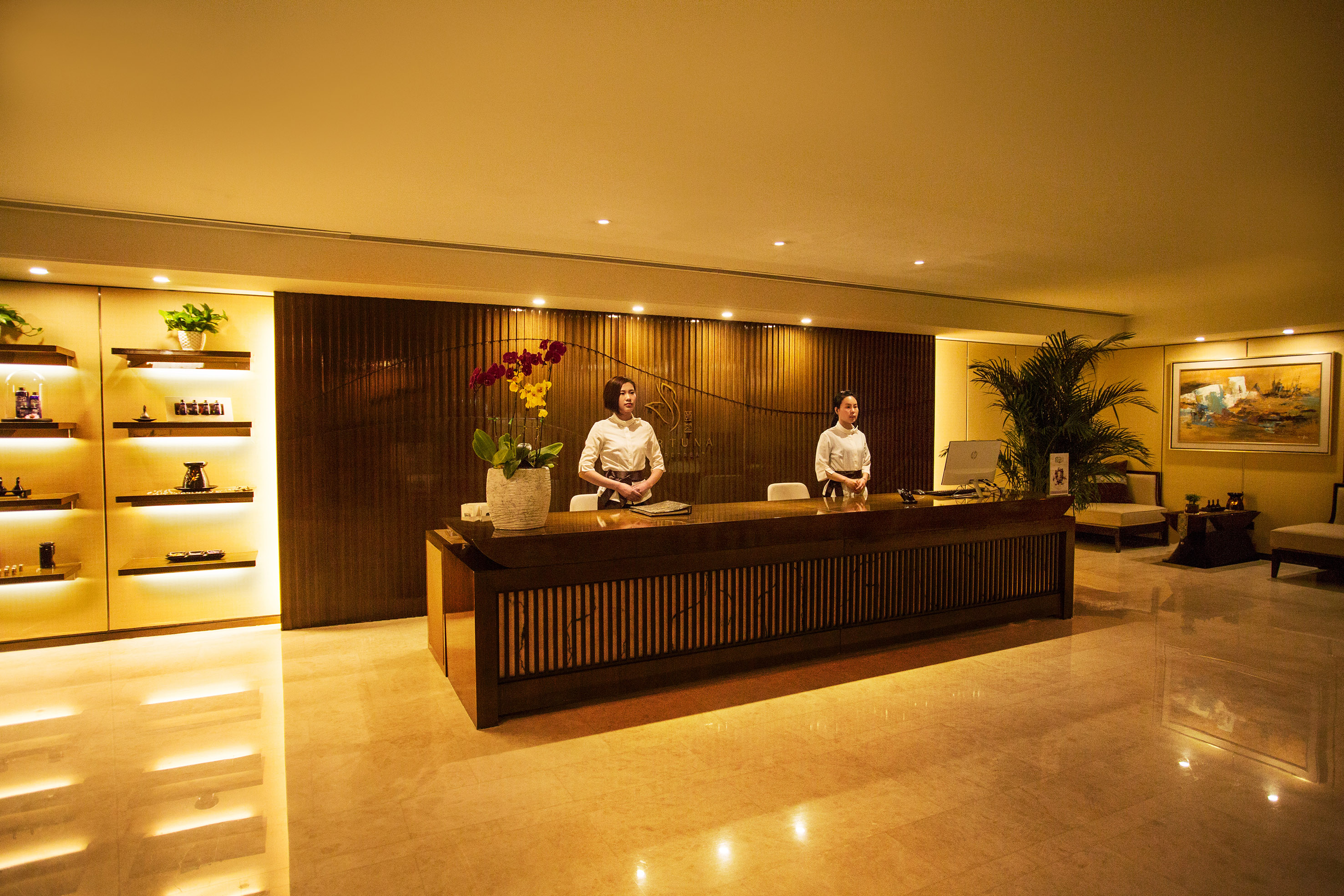 Two receptionists at warm spa reception desk with products and orchids.