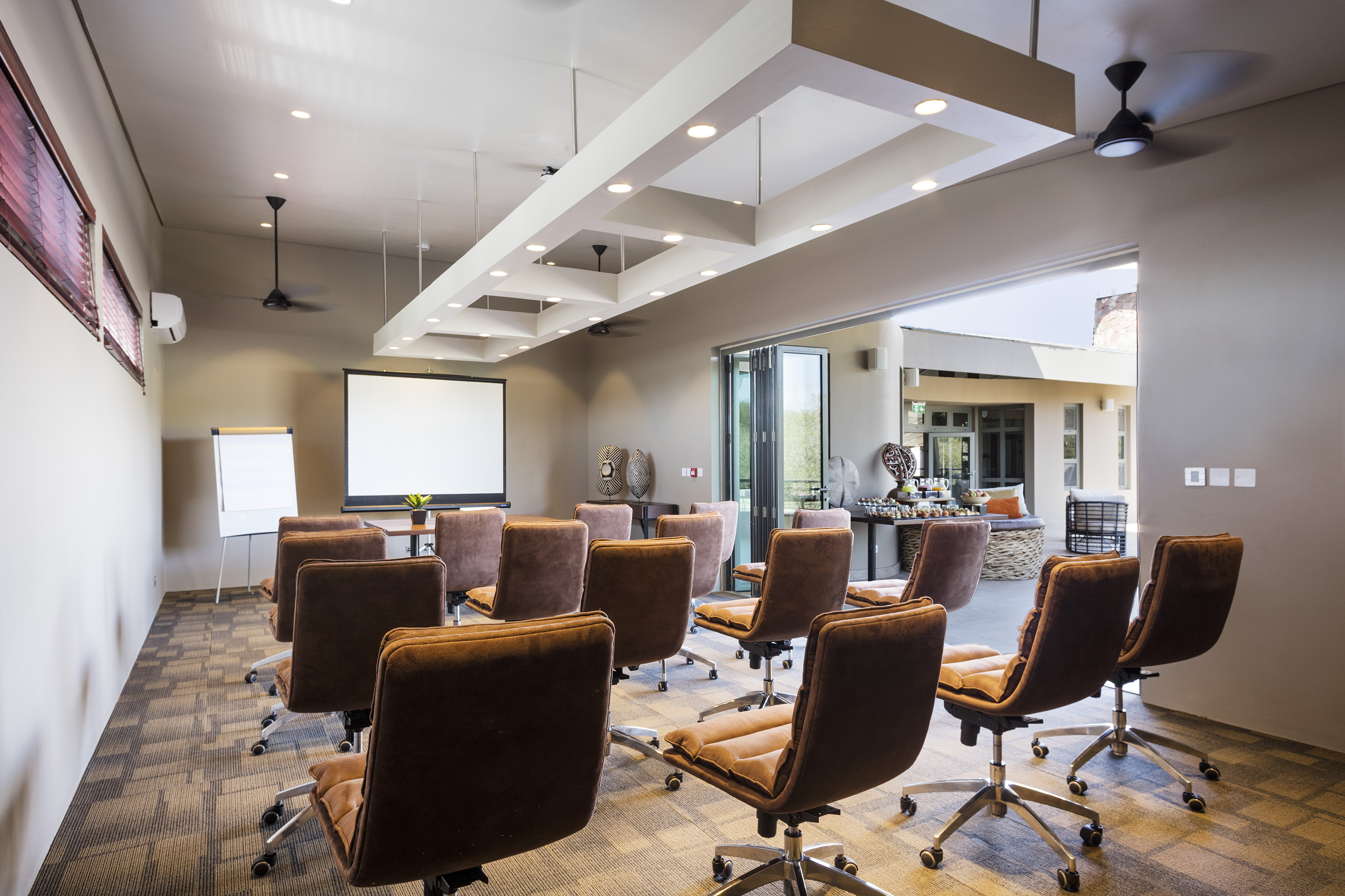 Modern conference room with brown chairs, projector screen, and outdoor area.
