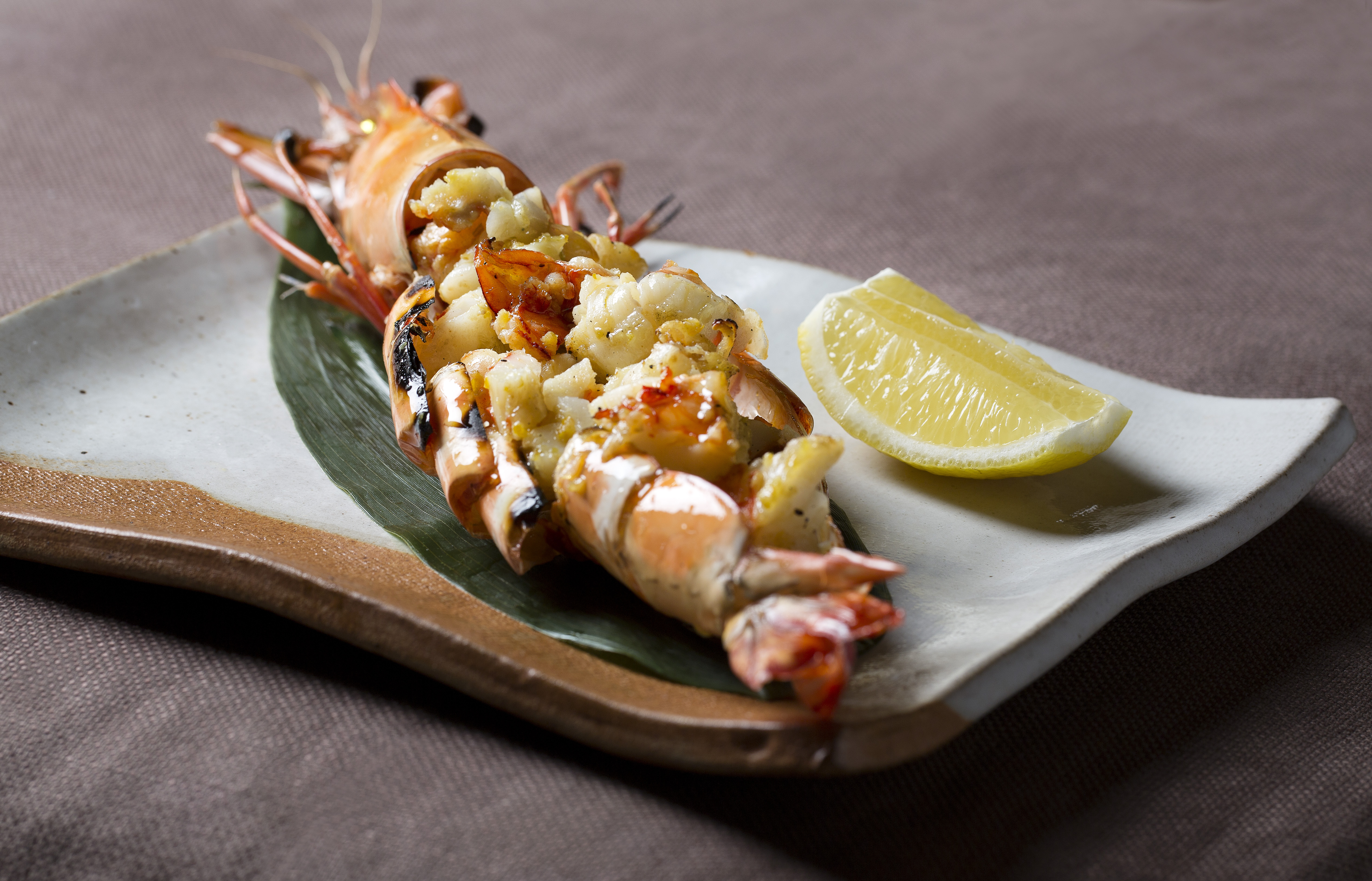 Grilled king prawn with savory stuffing and lemon on a ceramic plate.