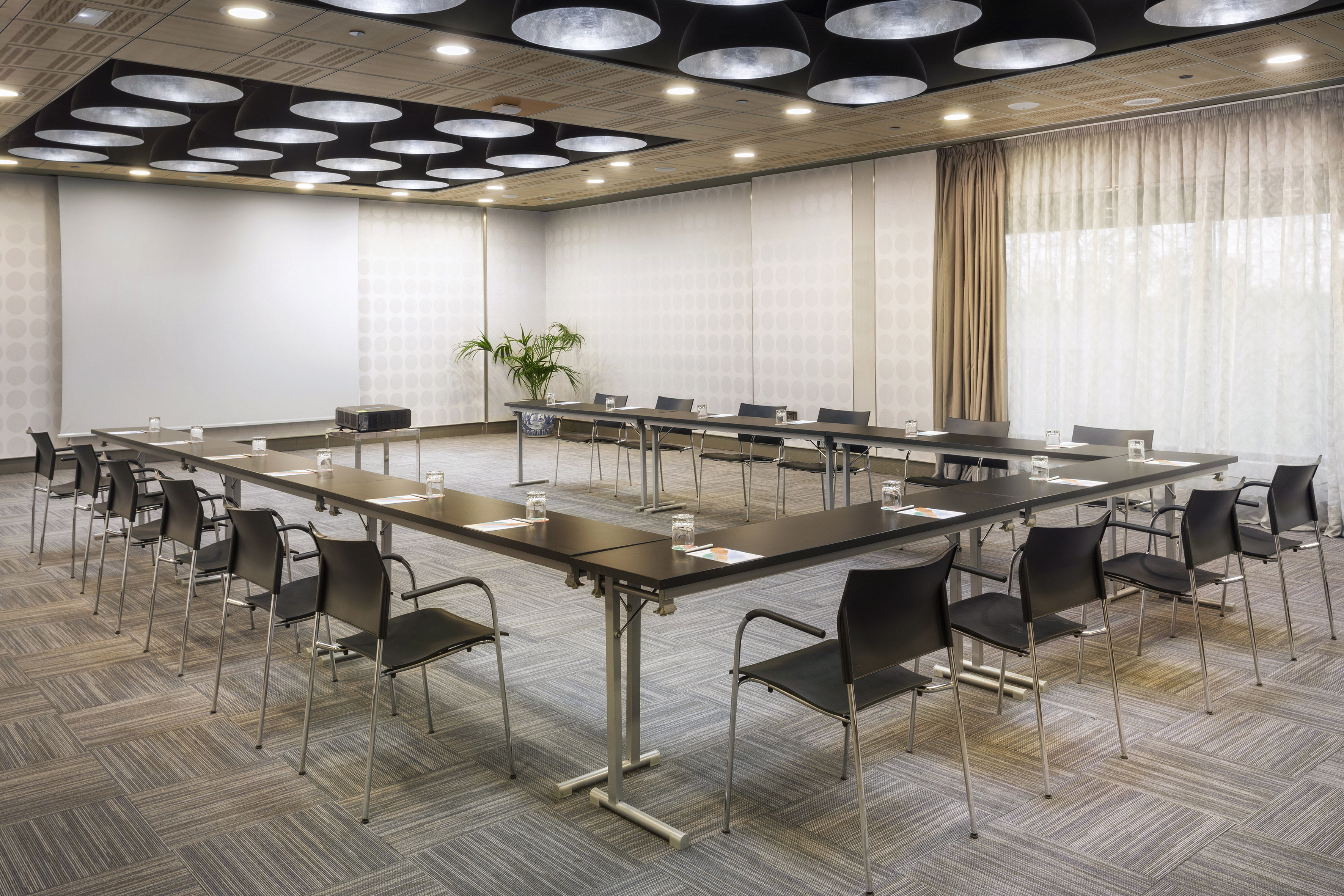 Modern conference room with U-shaped table, projector, screen, and chairs.