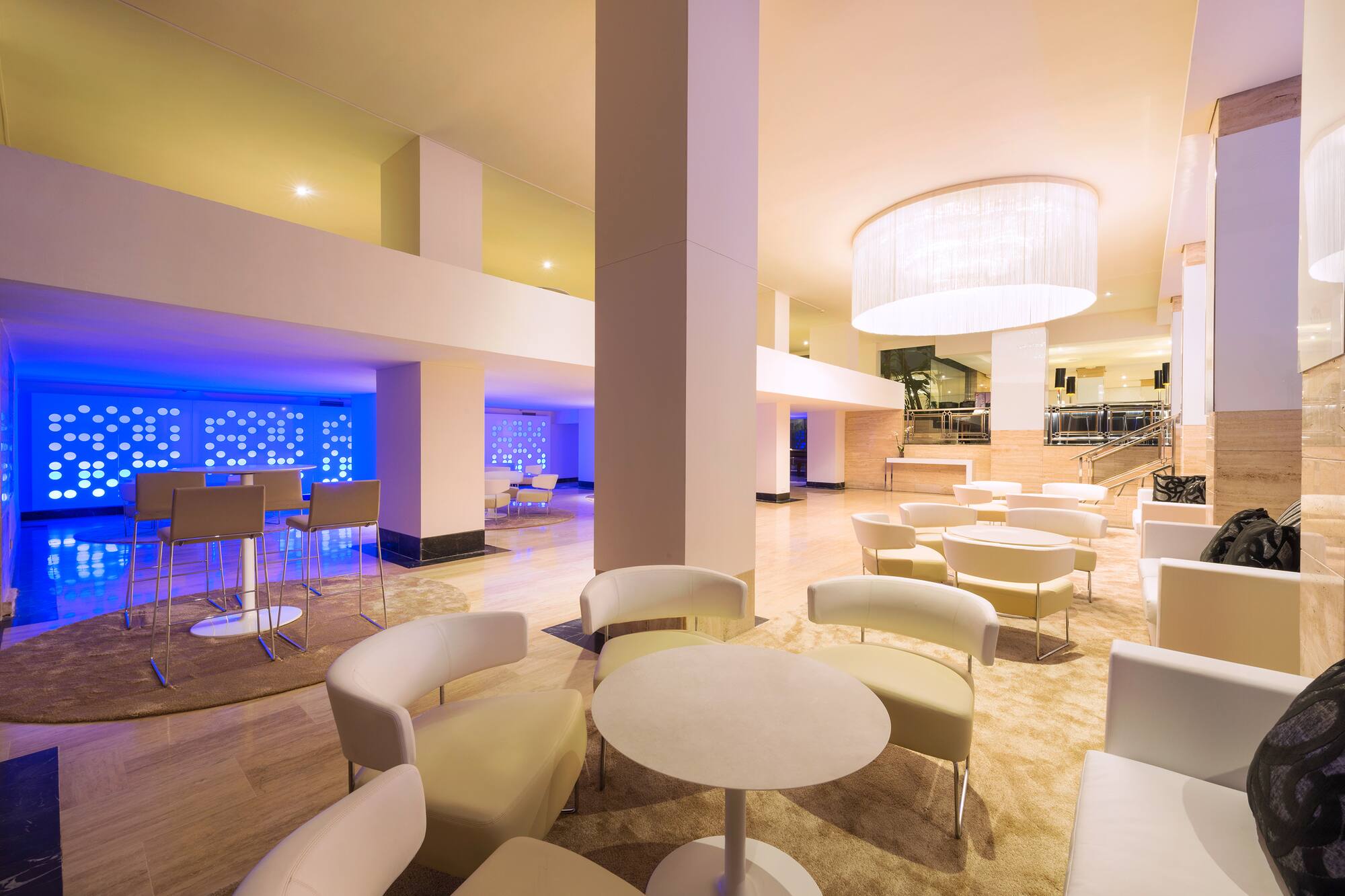 Modern hotel lounge with various seating, large chandelier, and blue accent bar.