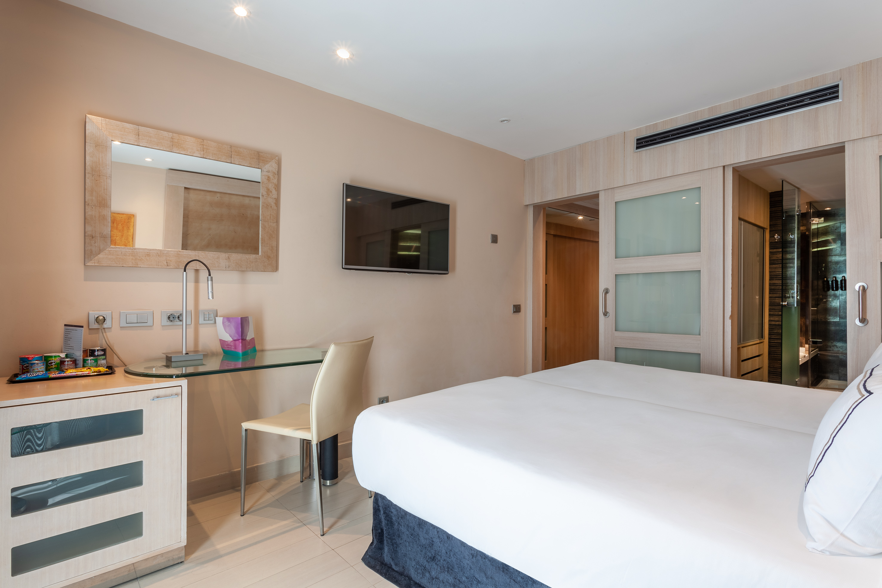 Modern hotel room with a large bed, workspace, and mounted TV.