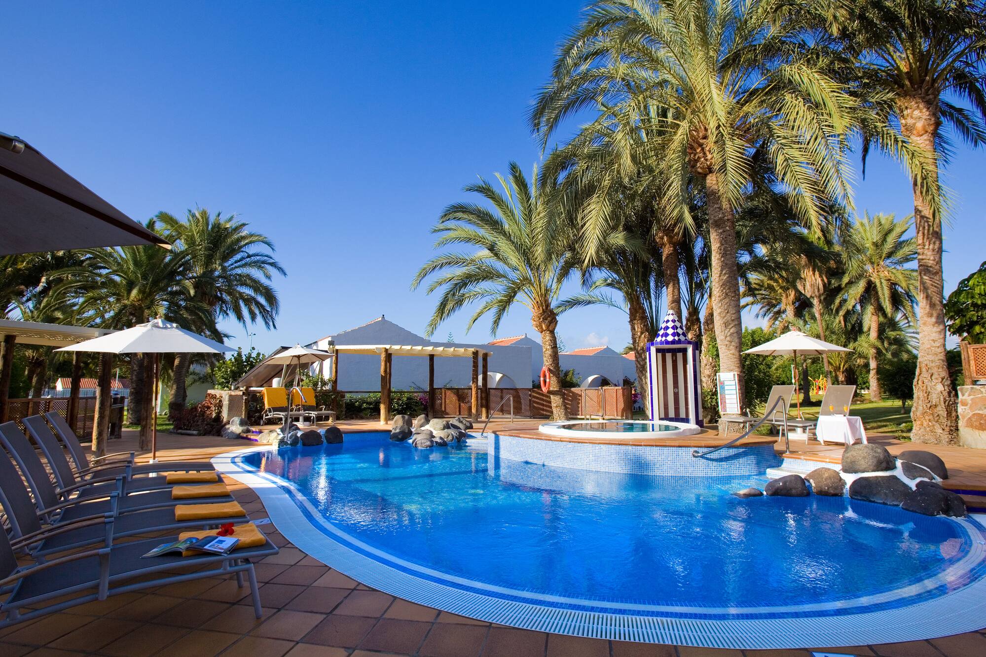 Tropical hotel swimming pool surrounded by palm trees and sun loungers.