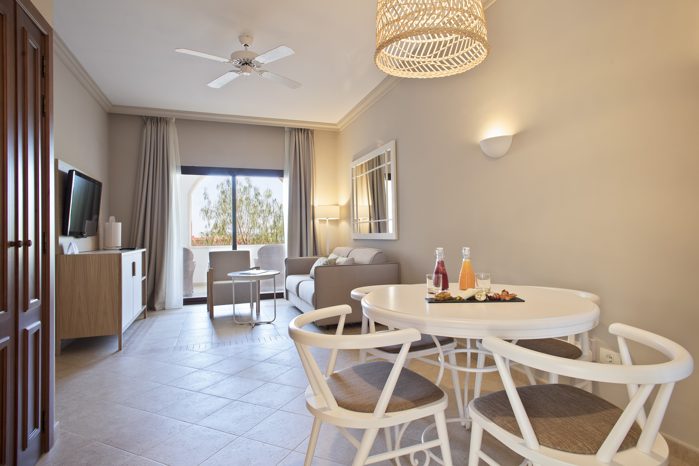 Bright hotel suite with dining table, sofa, and balcony access.