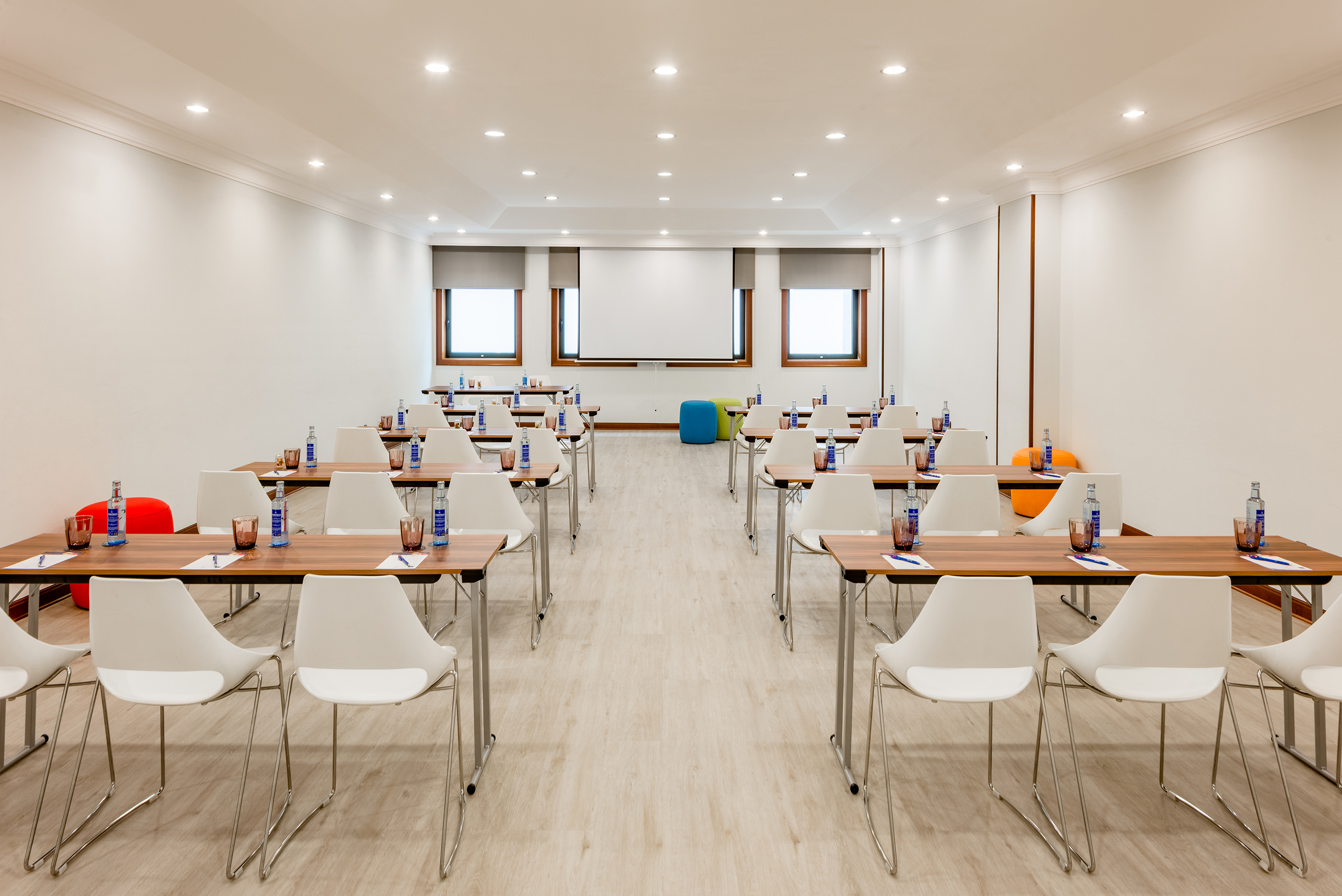 Modern training room with tables, white chairs, and projector screen. - Coruña - Hotel Santiago Plaza Affiliated by Meliá, Santiago de Compostela