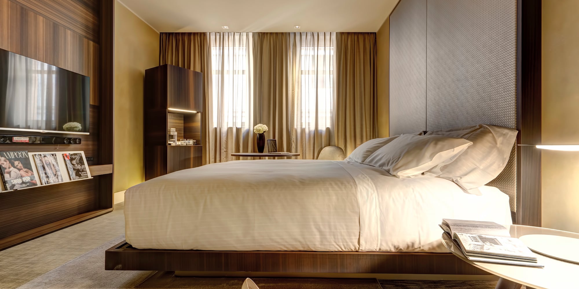 Modern luxury hotel bedroom with large bed, dark wood decor, and TV.