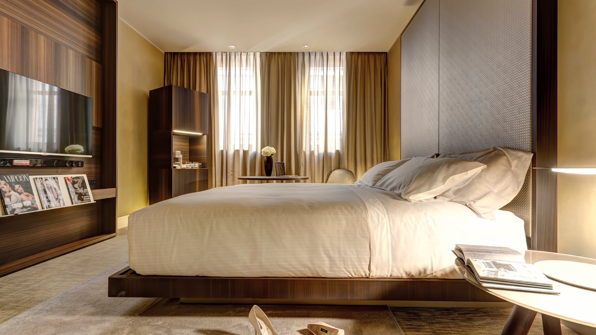 Modern luxury hotel bedroom with large bed, dark wood decor, and TV.