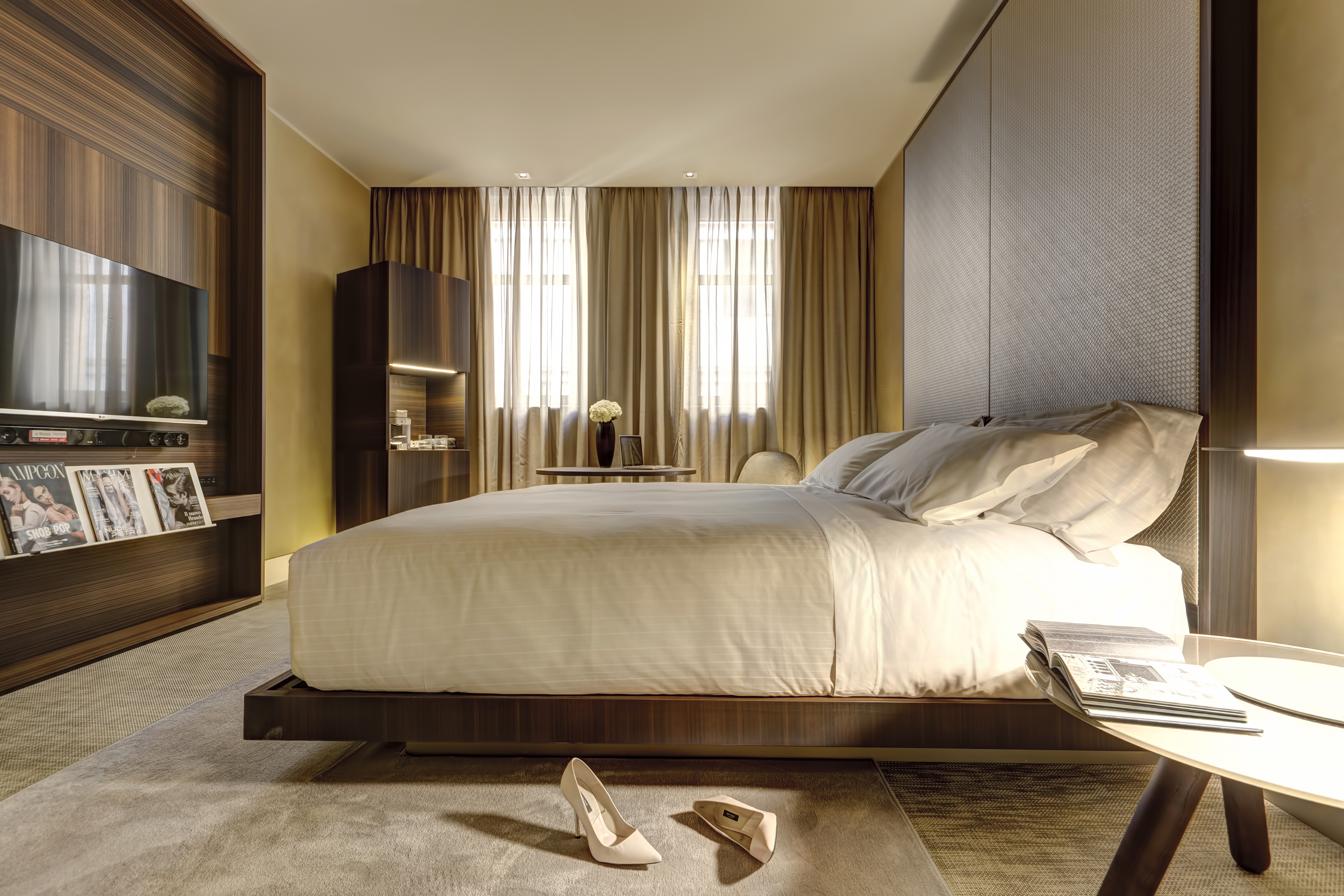 Modern luxury hotel bedroom with large bed, dark wood decor, and TV.