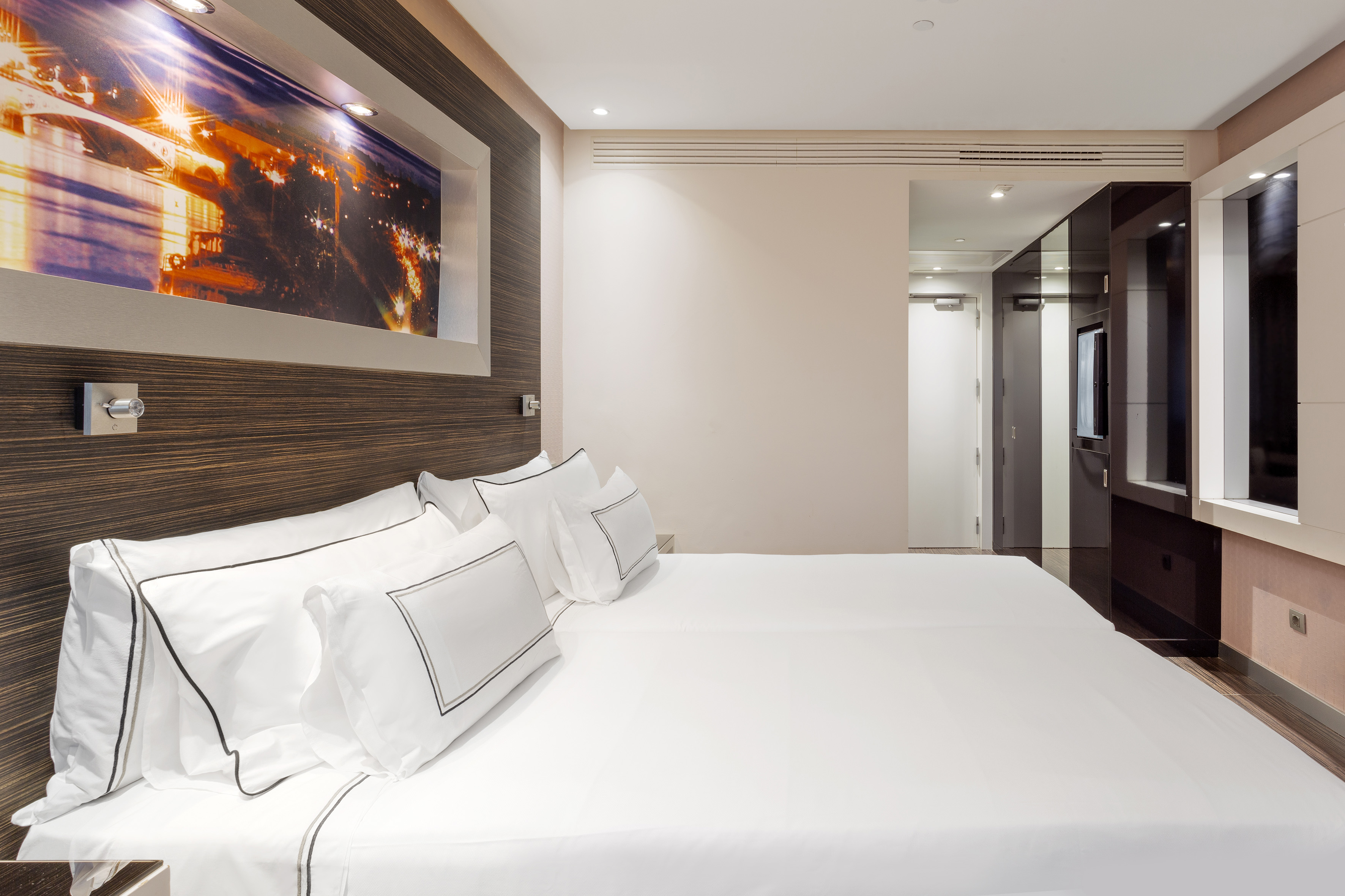 Clean, modern hotel room with twin beds, white bedding, and glowing city artwork.