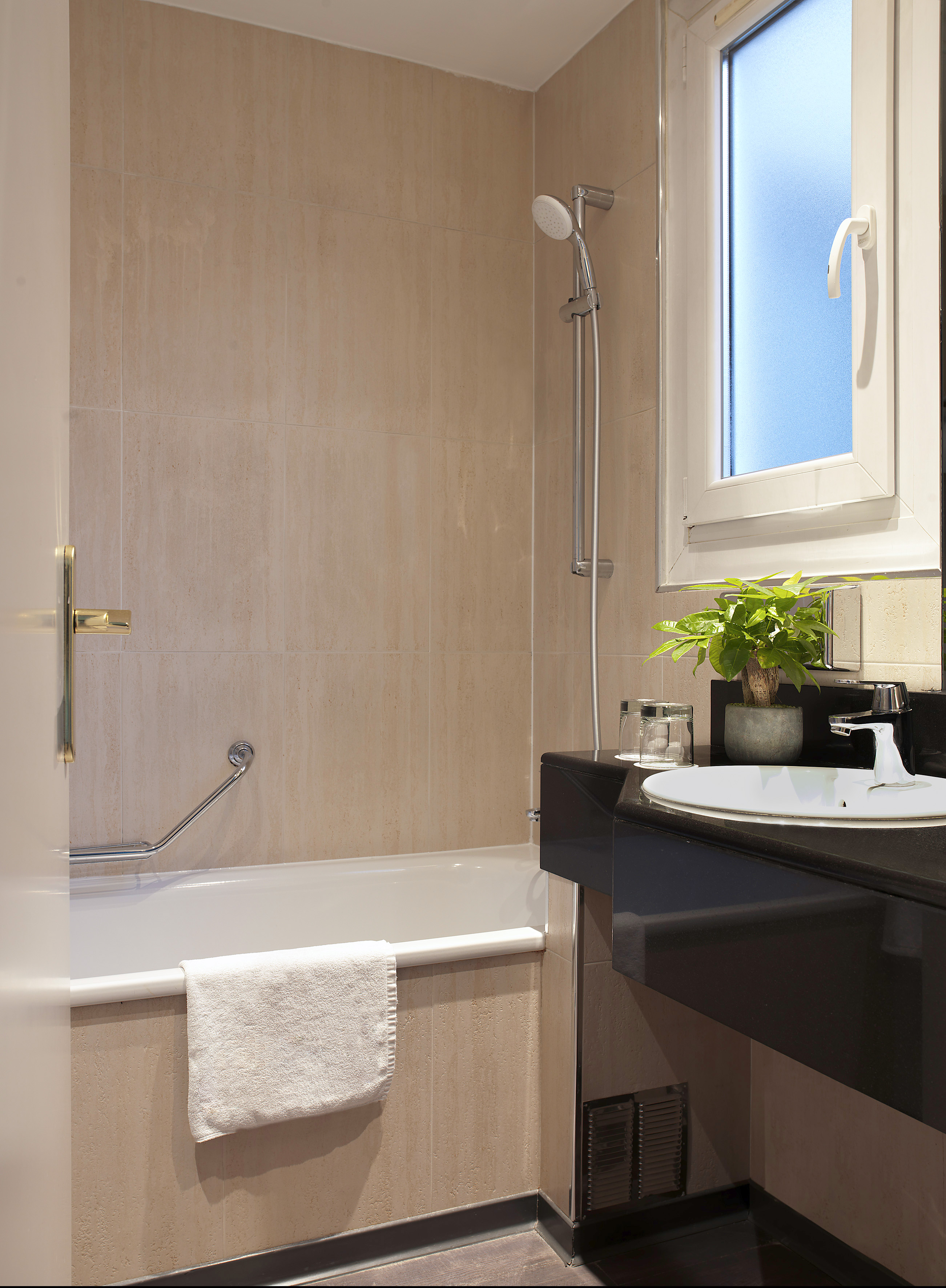 Hotel bathroom with bathtub, shower, dark vanity sink, and frosted window.