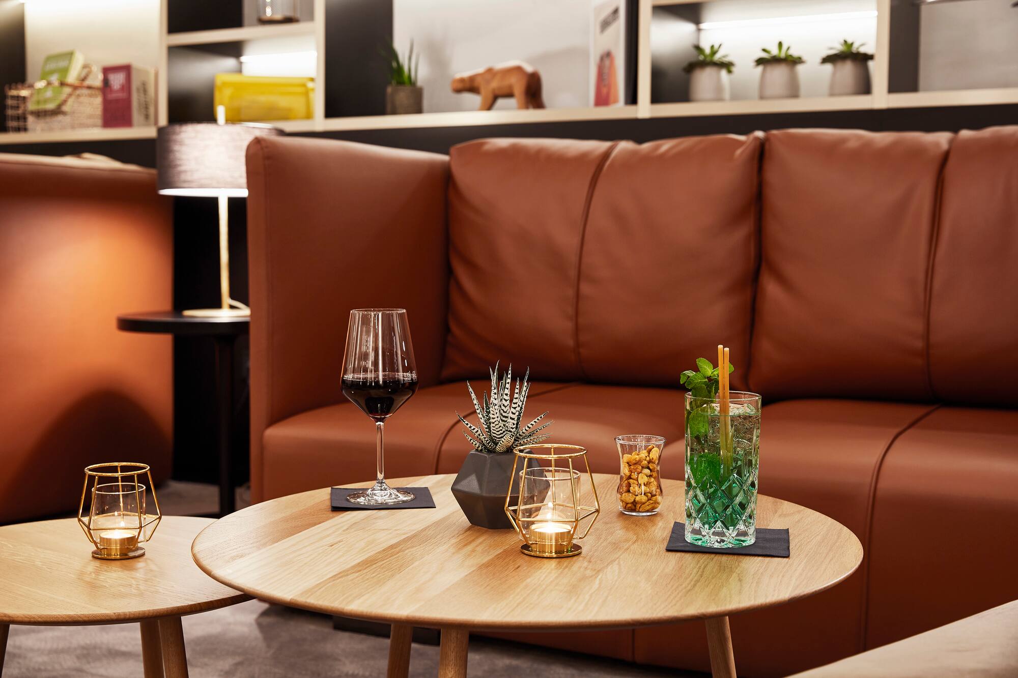 Modern lounge with brown leather sofa, wine, cocktail, and snacks on wooden tables.