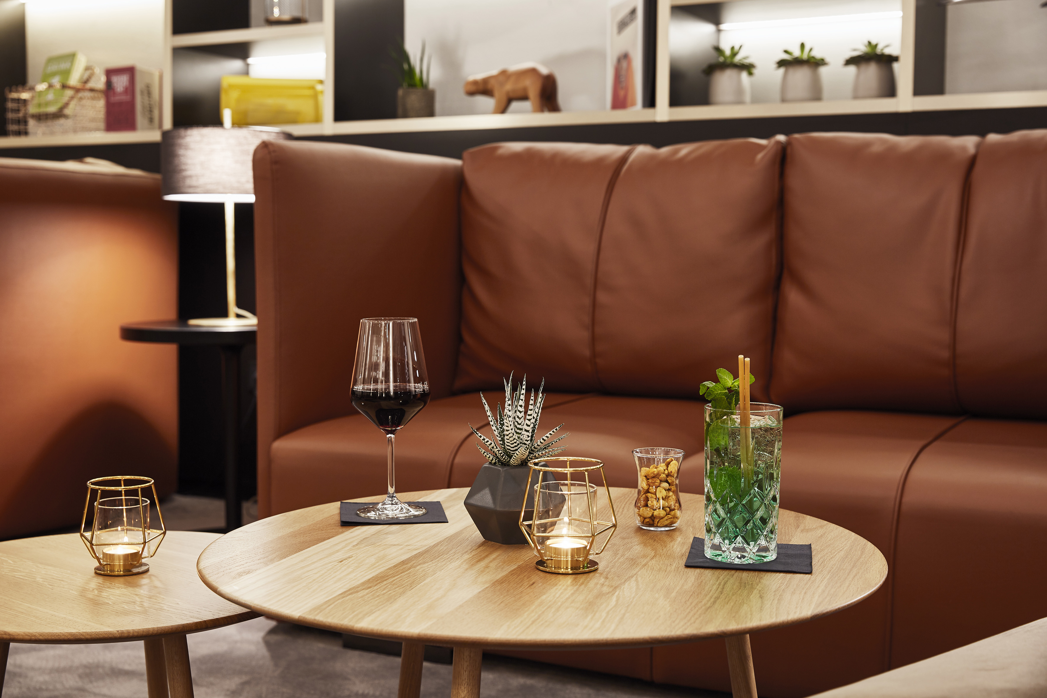 Modern lounge with brown leather sofa, wine, cocktail, and snacks on wooden tables.