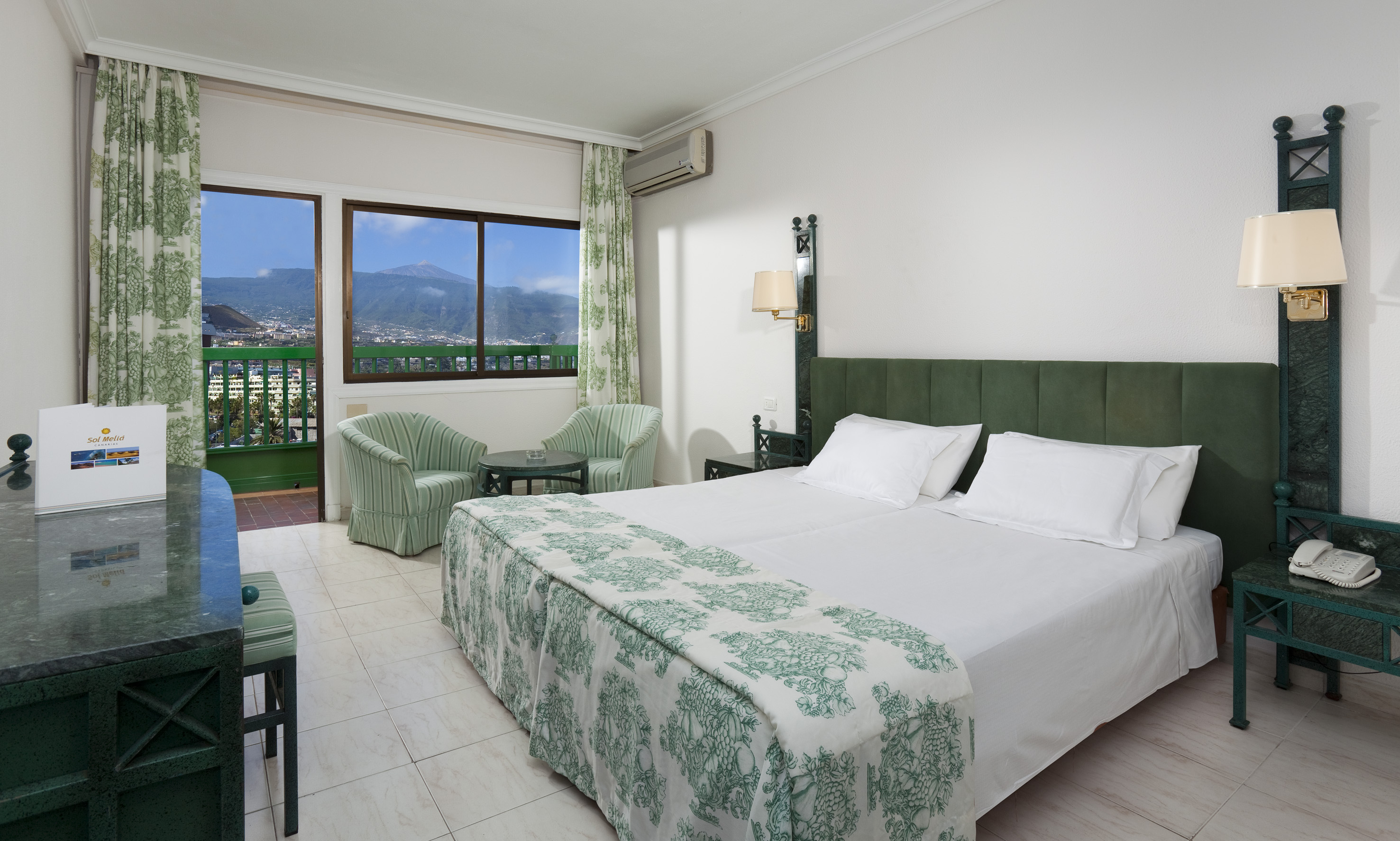 Hotel room with twin beds, mountain view balcony, and green decor.
