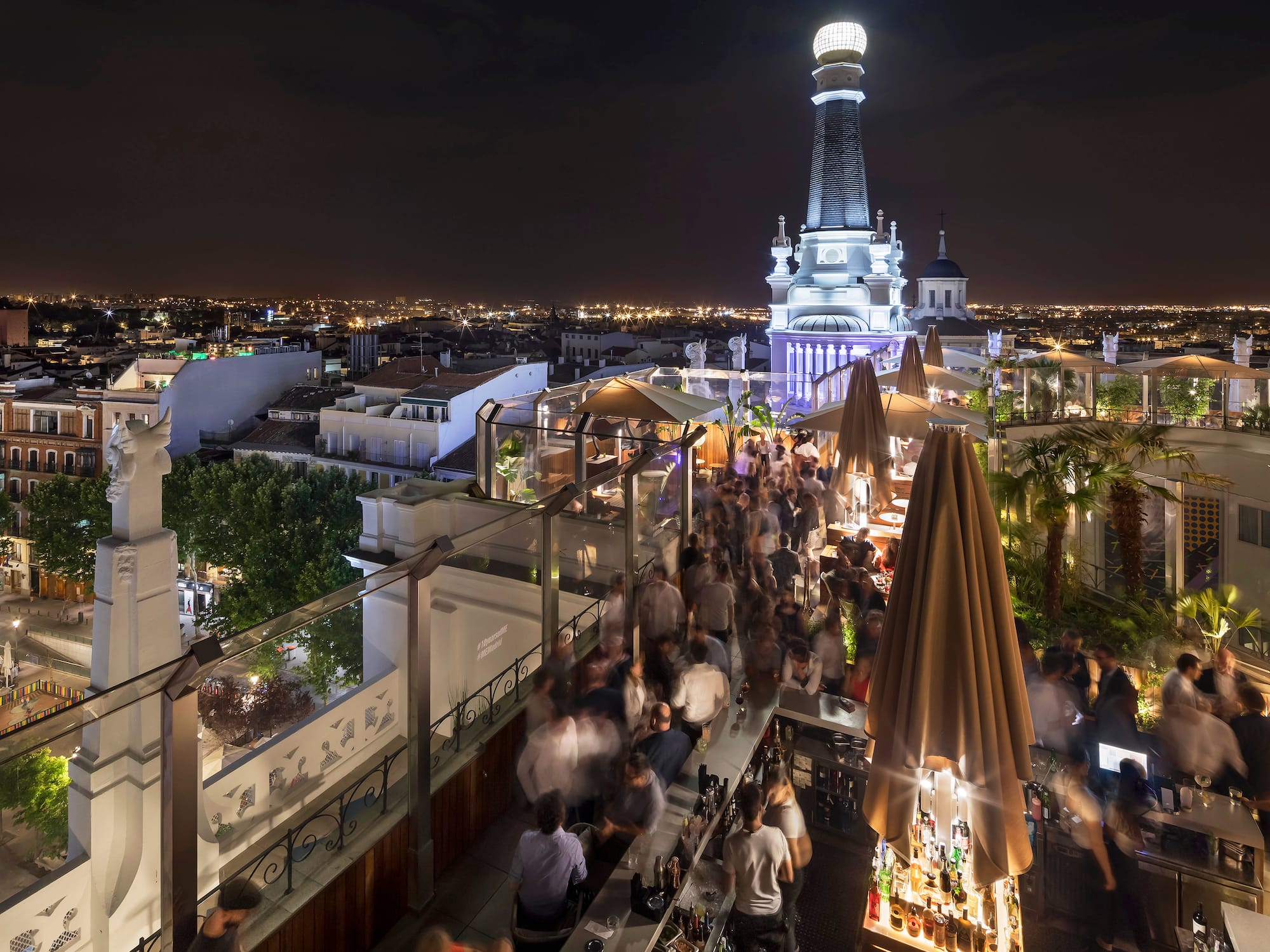 A group of individuals sitting on a rooftop, with a tall tower rising in the background.