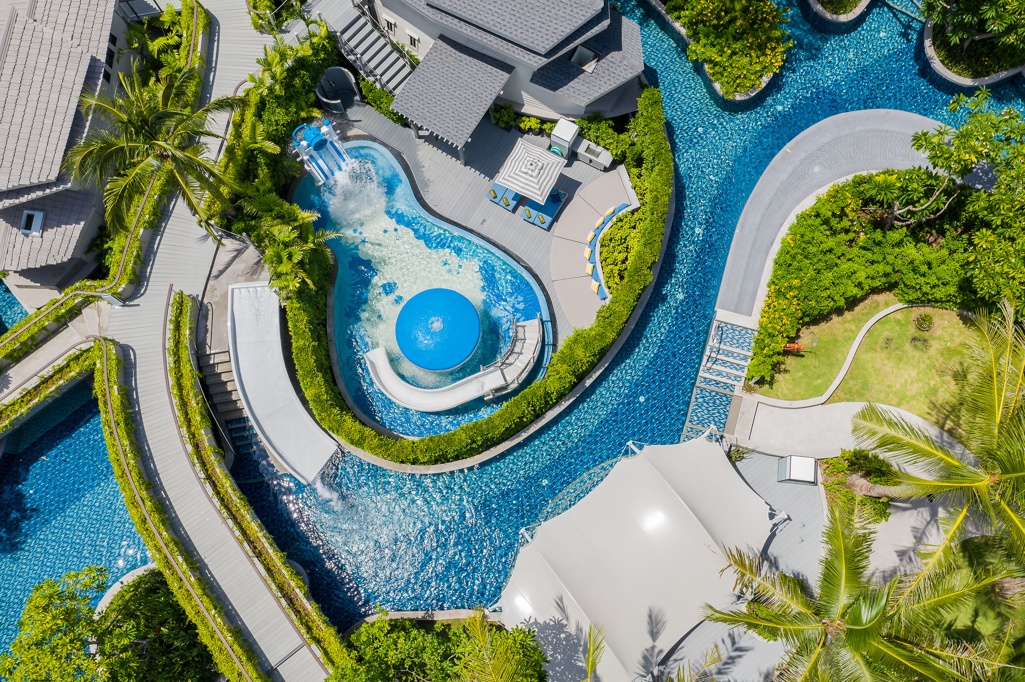 Aerial view luxury resort with winding pools, water slides, lazy river, palm trees.