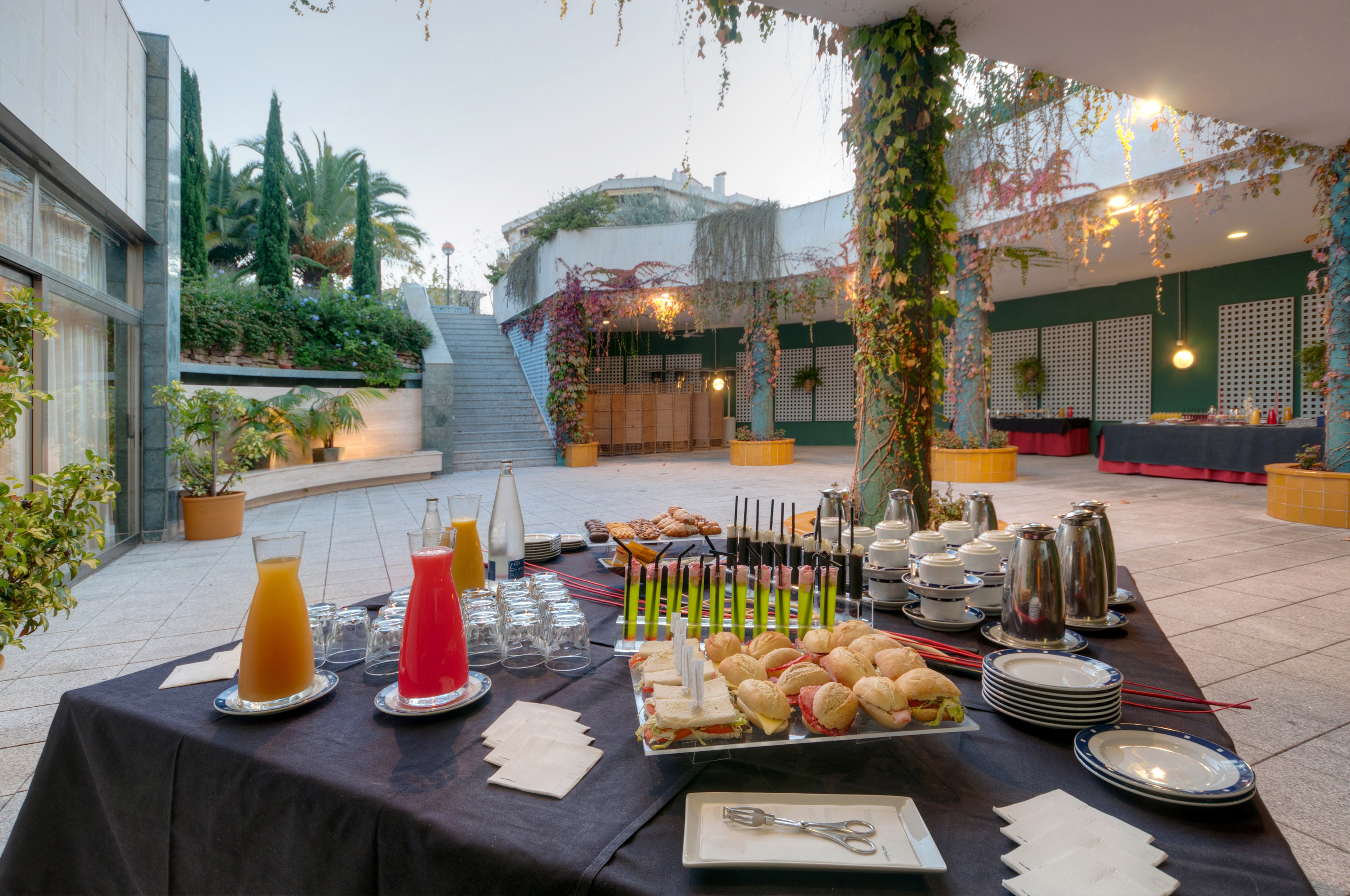 Outdoor event buffet with sandwiches, juices, coffee on a modern patio.