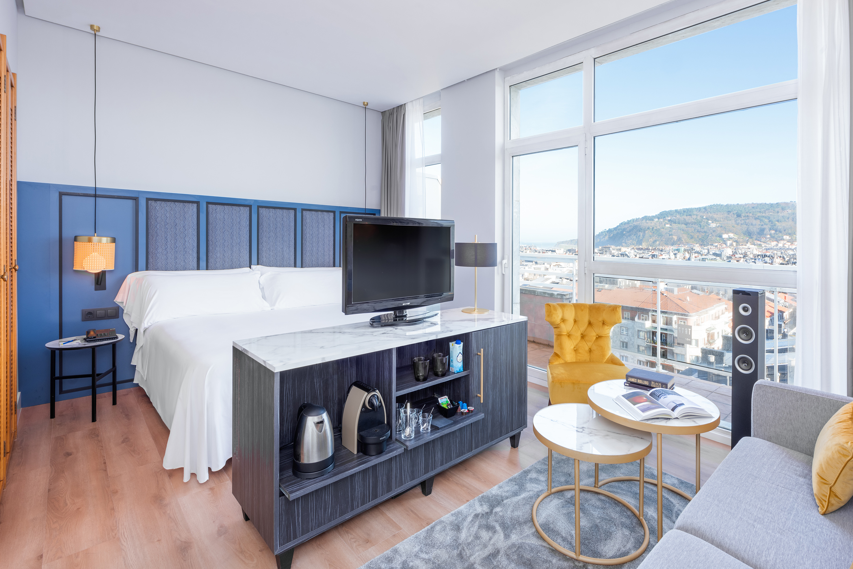 Modern hotel room with king bed, city and ocean view, TV, and seating area.
