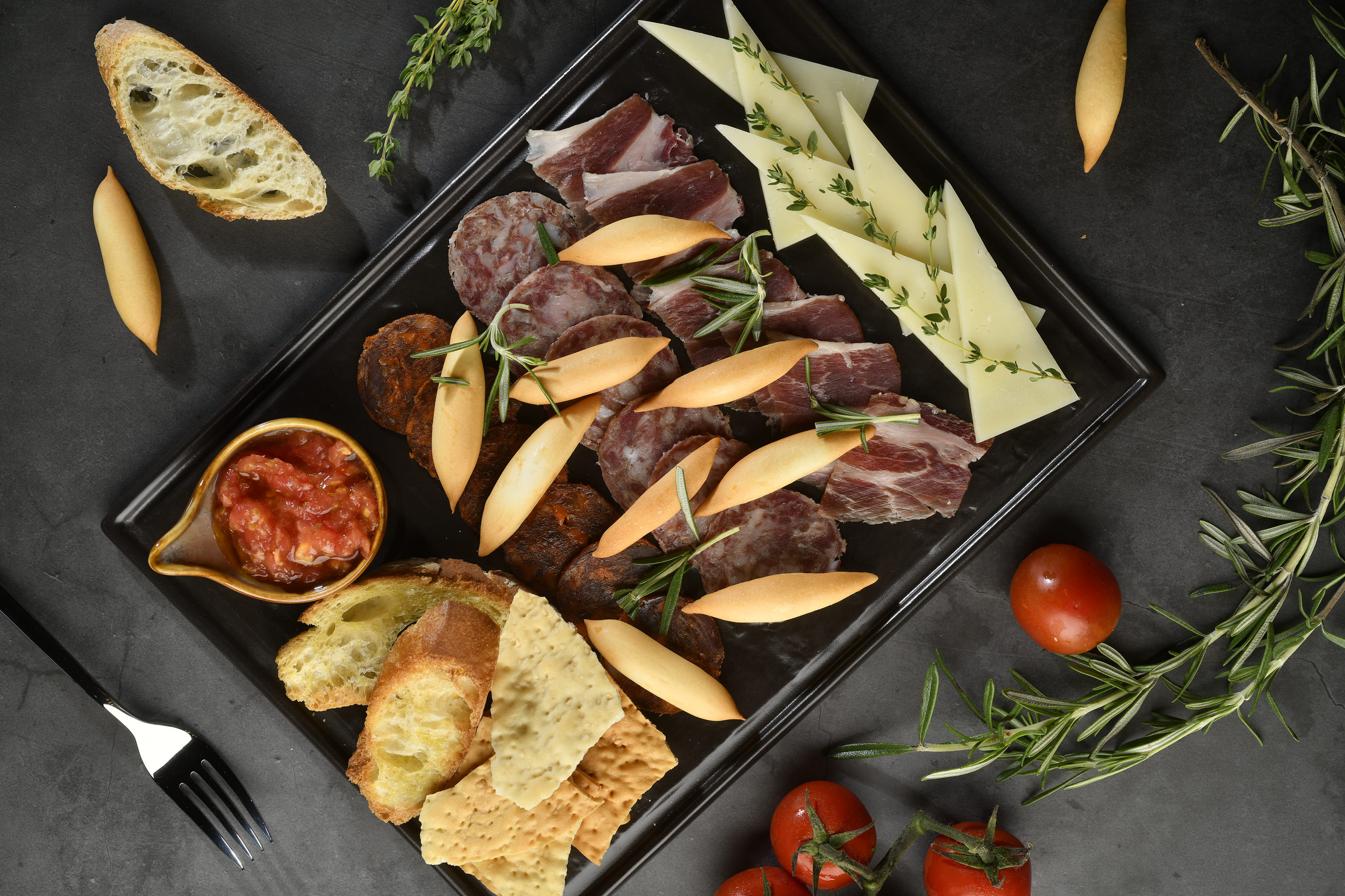 Tapas board with sliced meats, cheese, bread, tomato salsa, and fresh rosemary.
