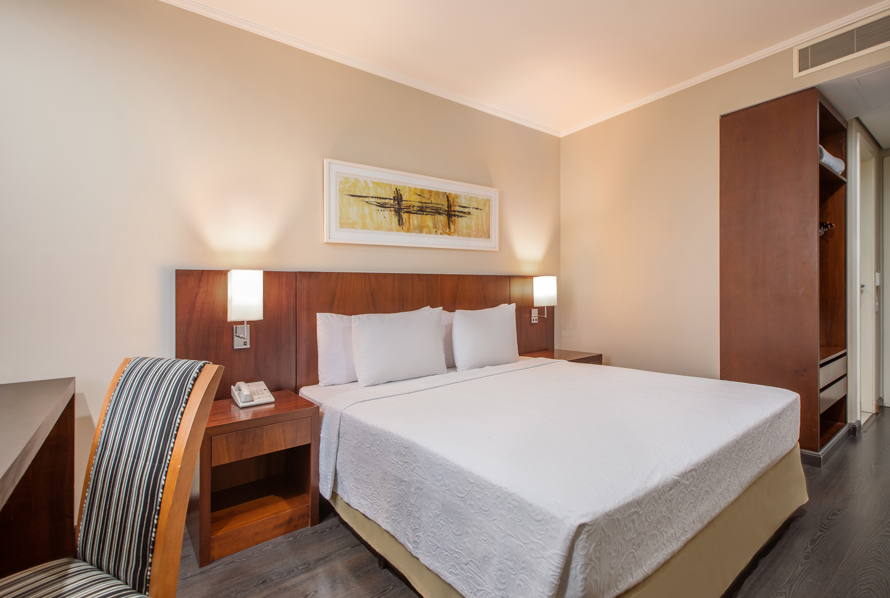 Hotel guest room with bed, bedside tables, desk, and modern decor.