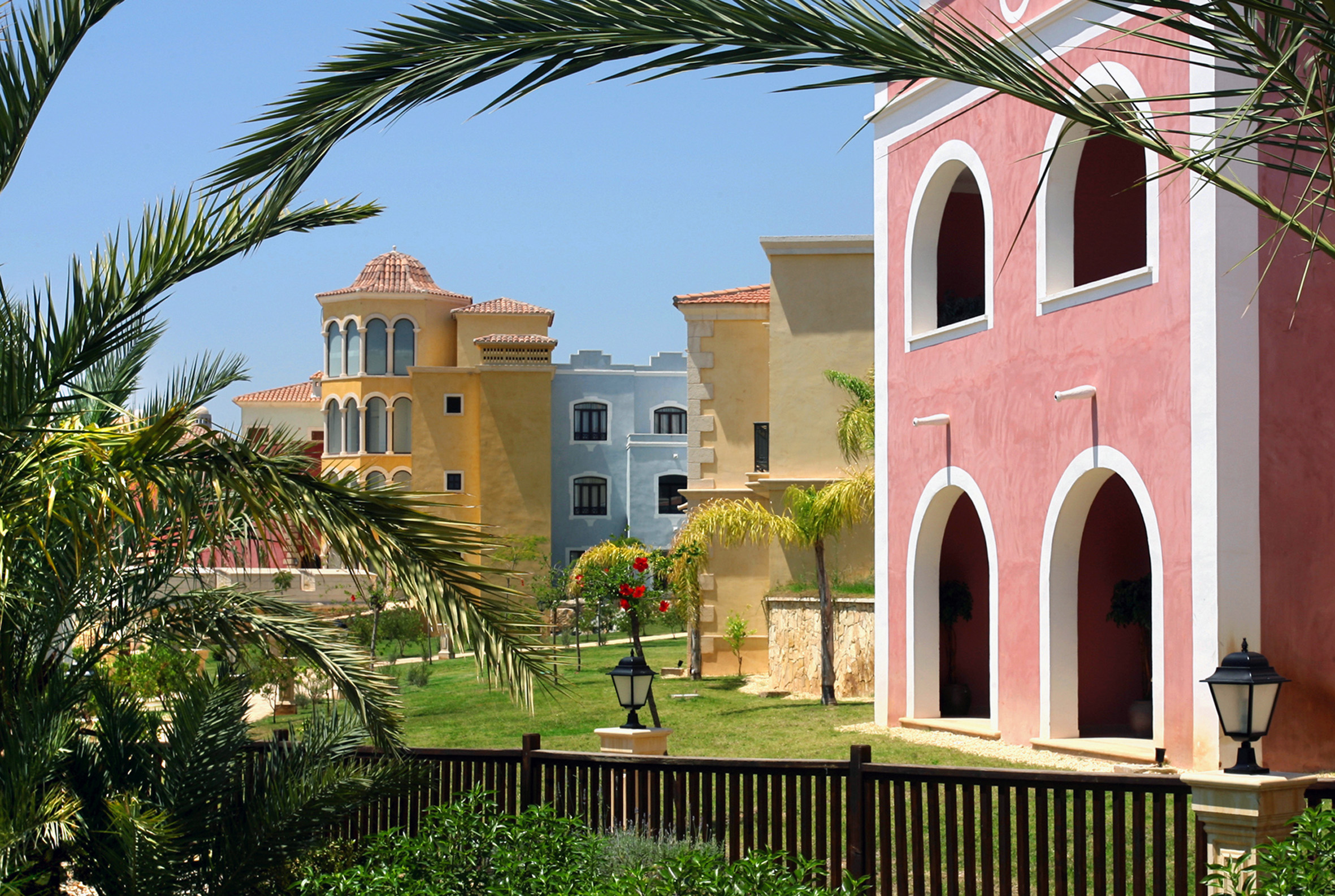 Vibrant Mediterranean resort villas framed by palm trees and green landscape.