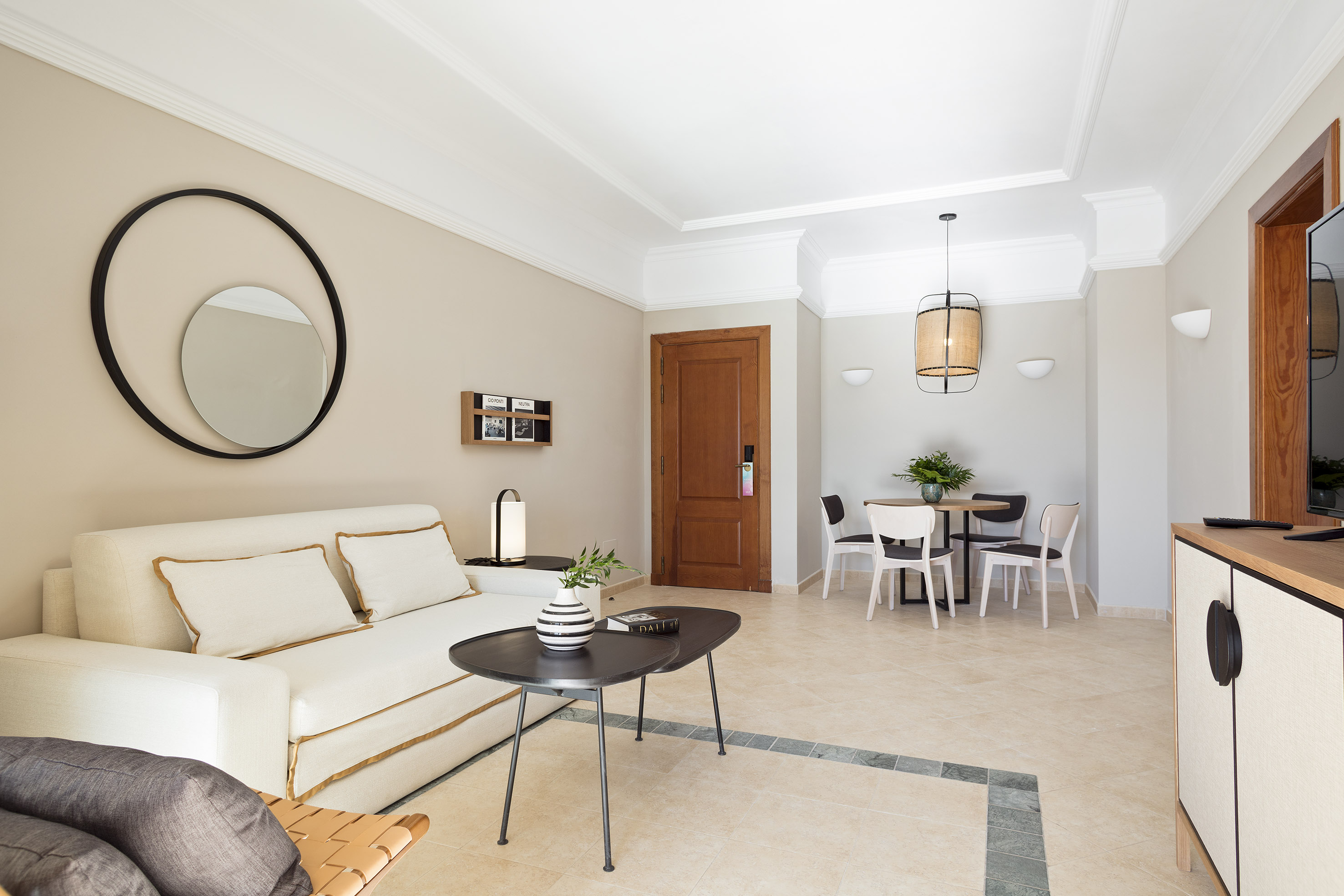 Modern living-dining room with white sofa, circular mirror, and neutral decor.