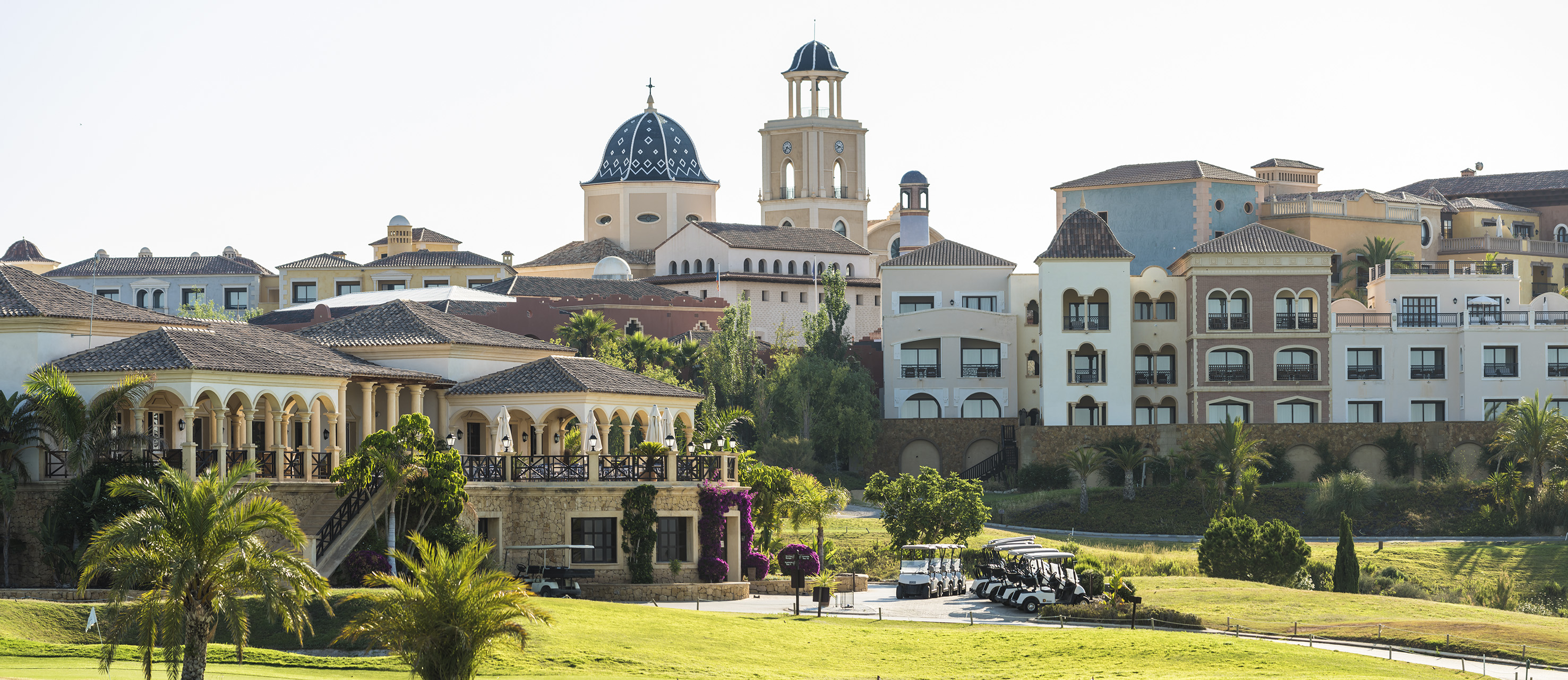 Mediterranean golf resort with traditional buildings, lush course, and bell tower.