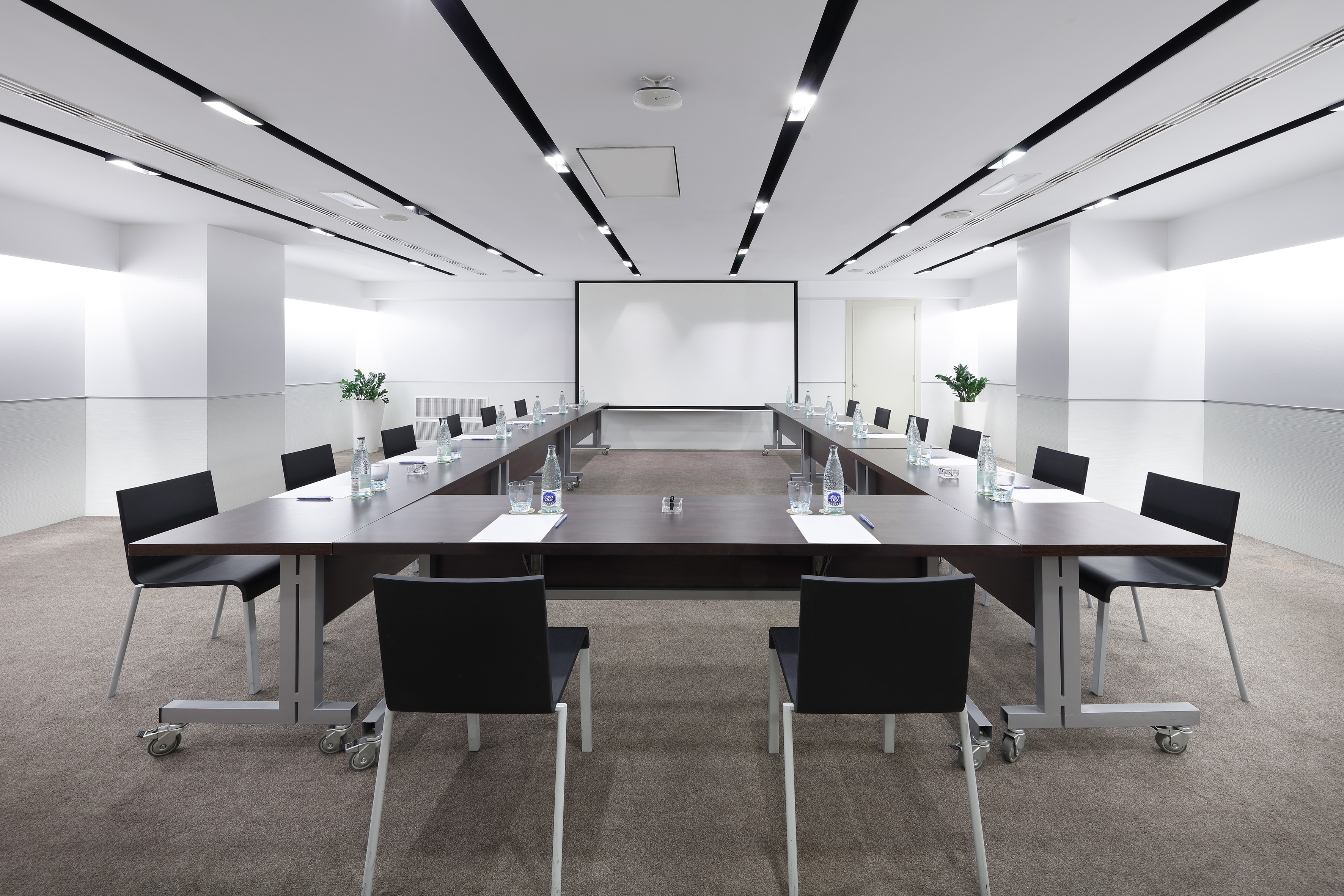 Modern corporate meeting room with U-shape table setup and projector screen.
