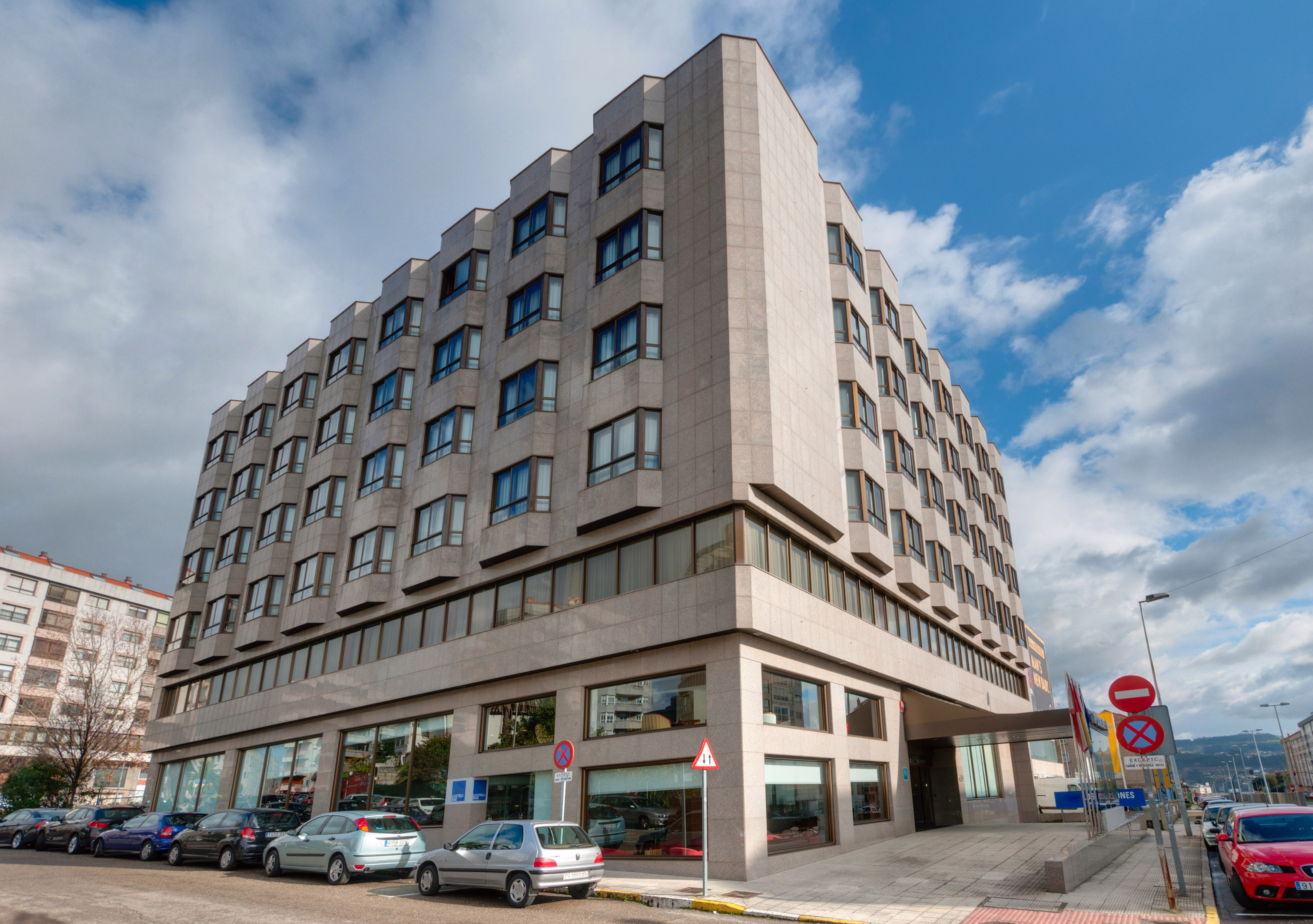 Modern hotel building facade with light stone, many windows, and parked cars.
