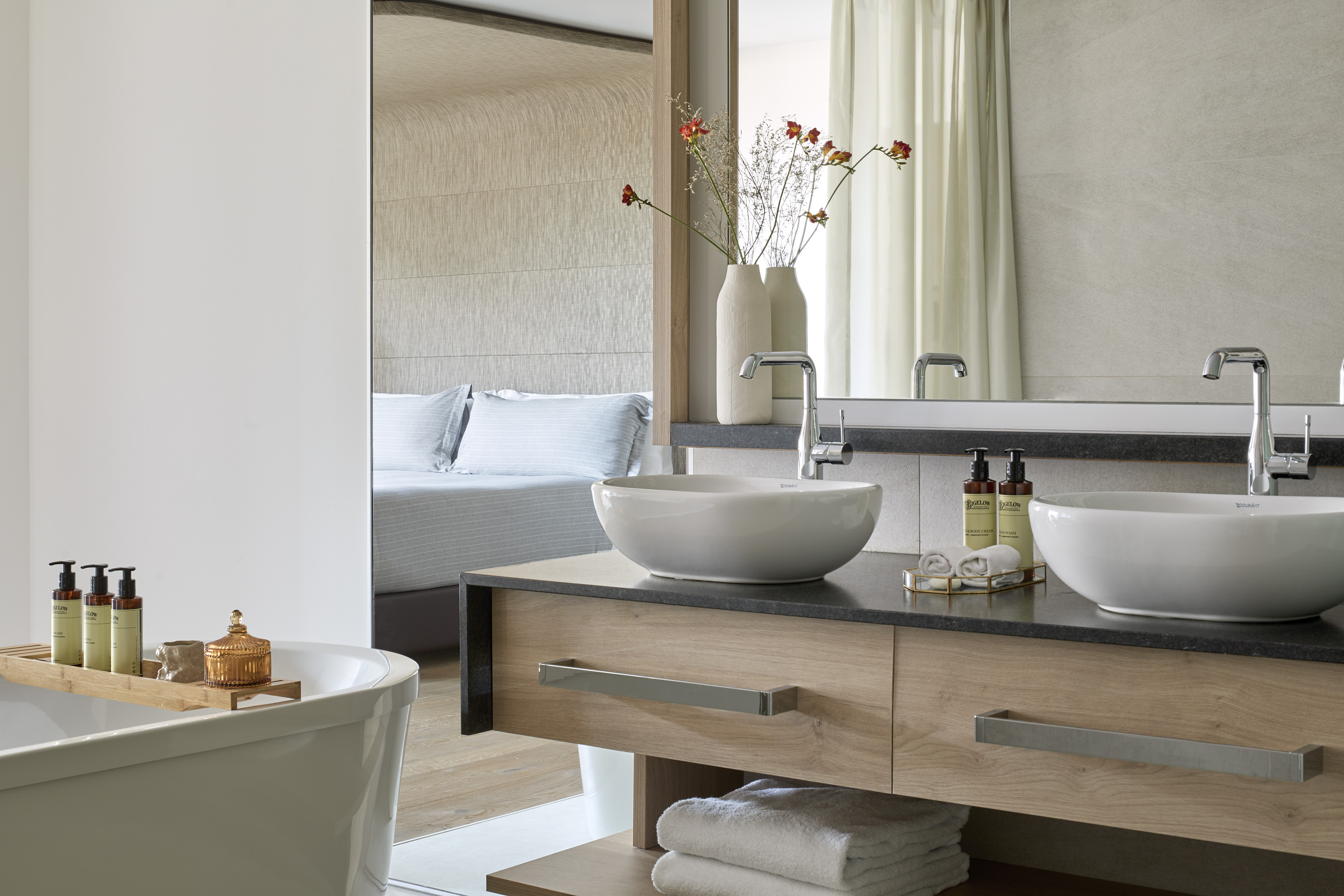 Luxury bathroom with double vessel sinks, soaking tub, and bedroom view.