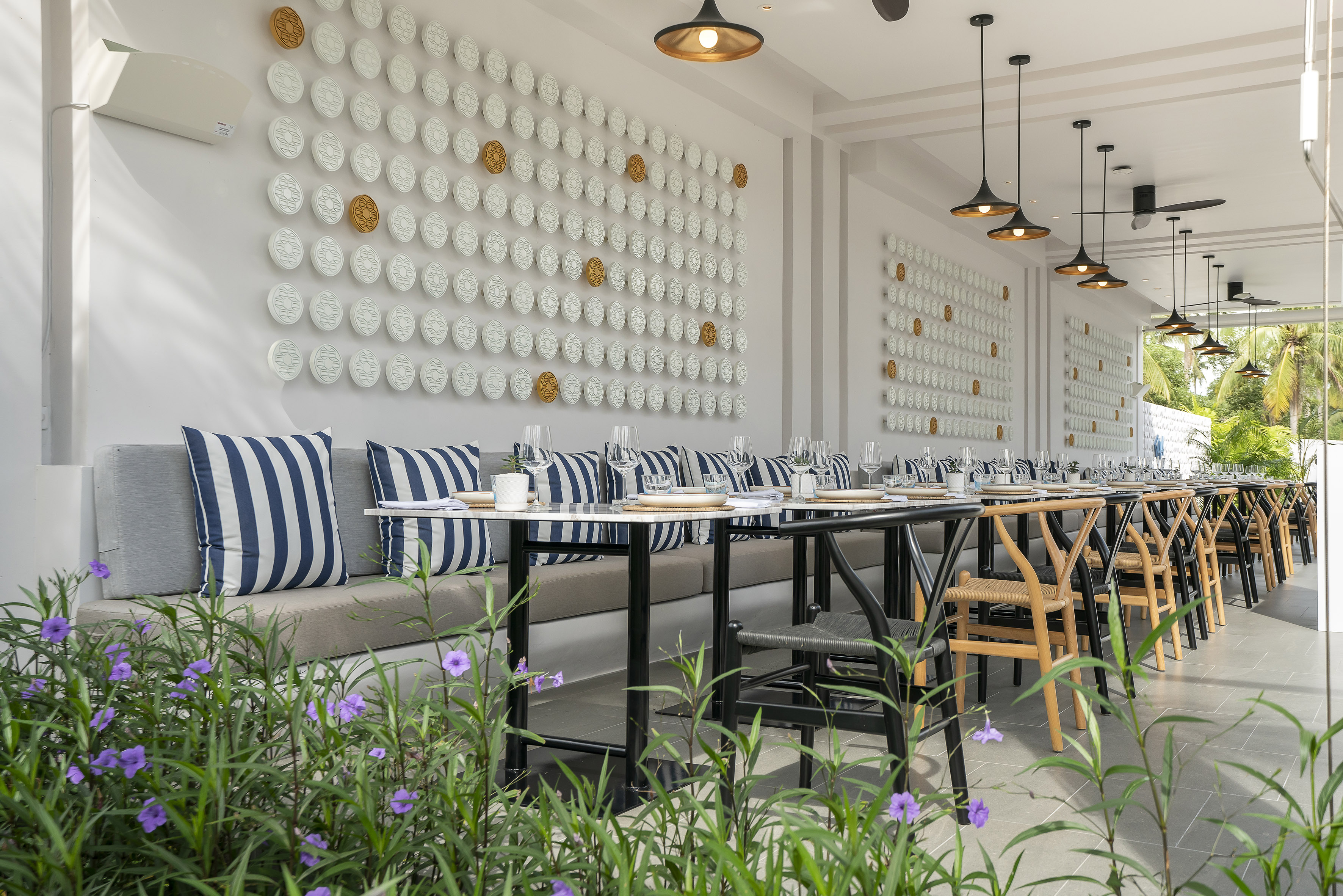 Outdoor resort dining with white decor wall, striped cushions, and set tables.