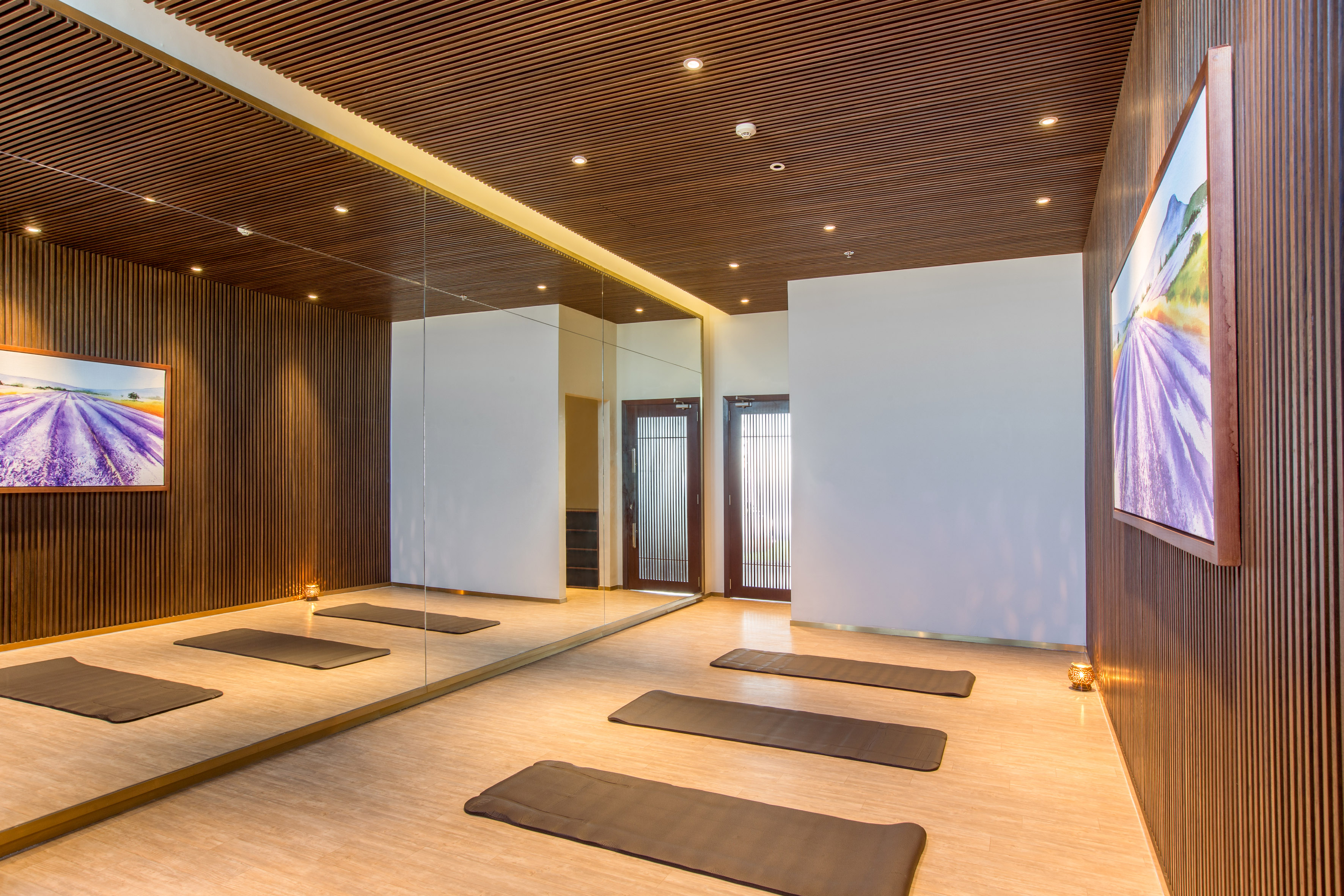 Empty modern yoga studio with wooden panels, large mirrors, and mats.