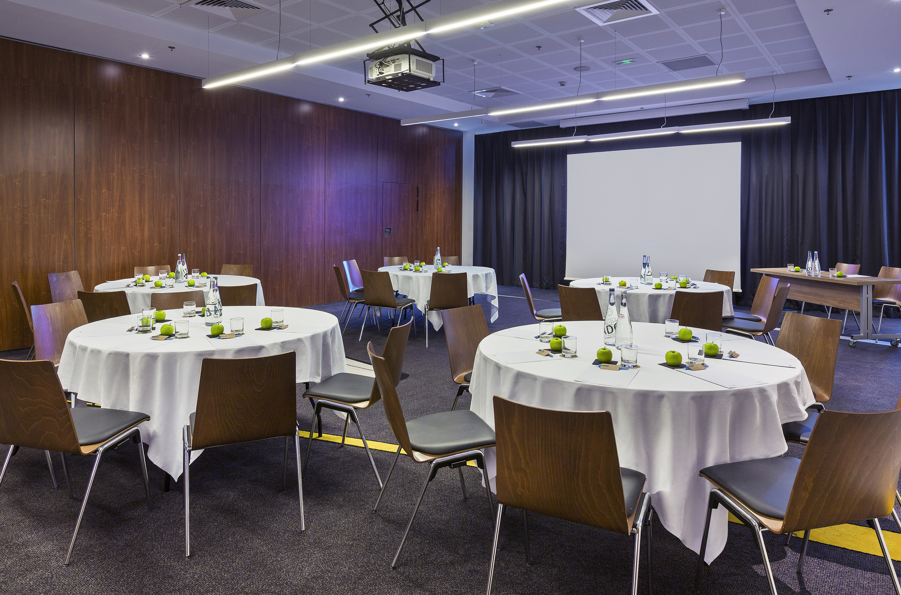 Modern conference room with round tables, chairs, projector, and screen.