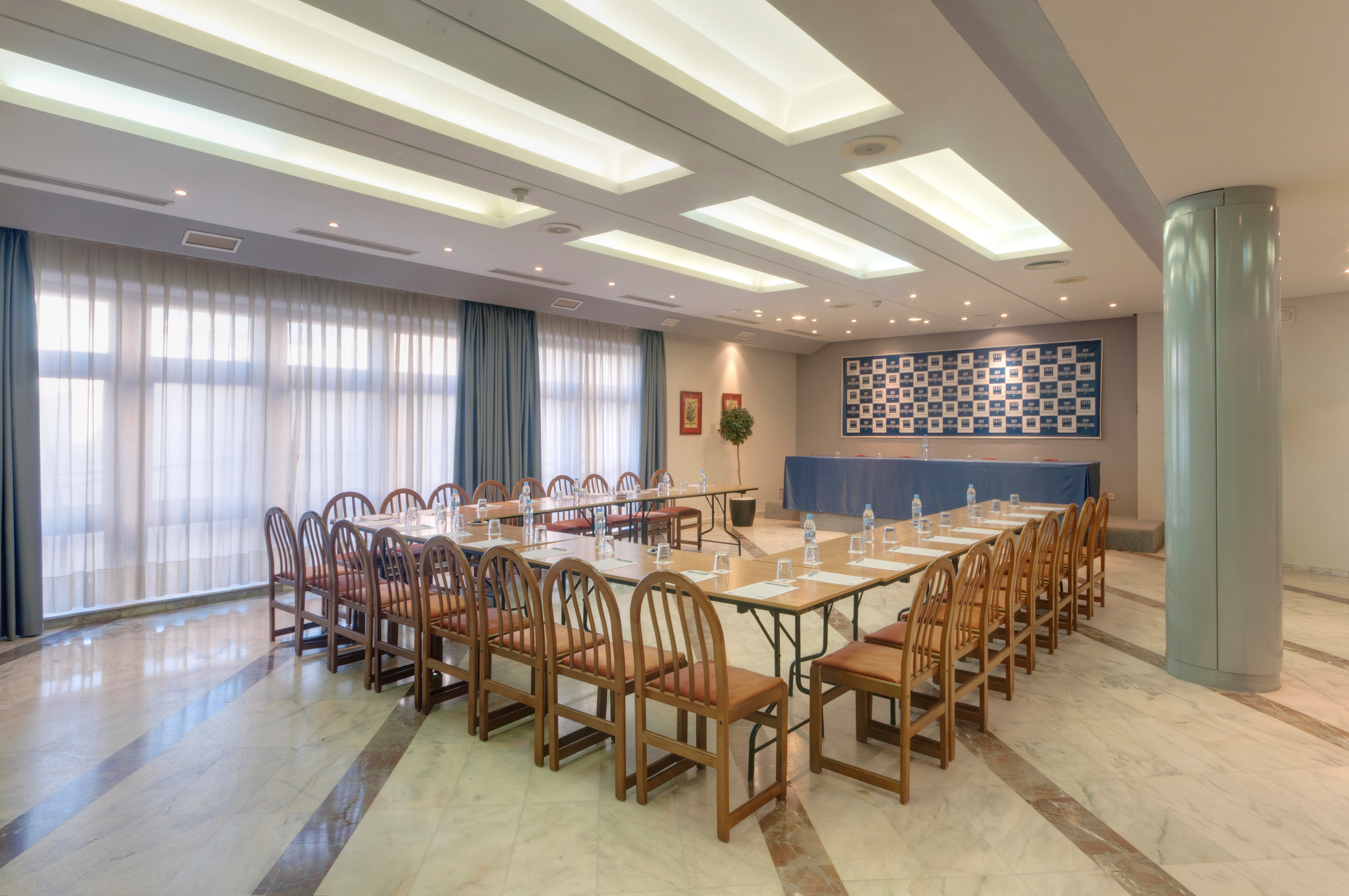 Bright conference room with U-shaped table, wooden chairs, and large windows.