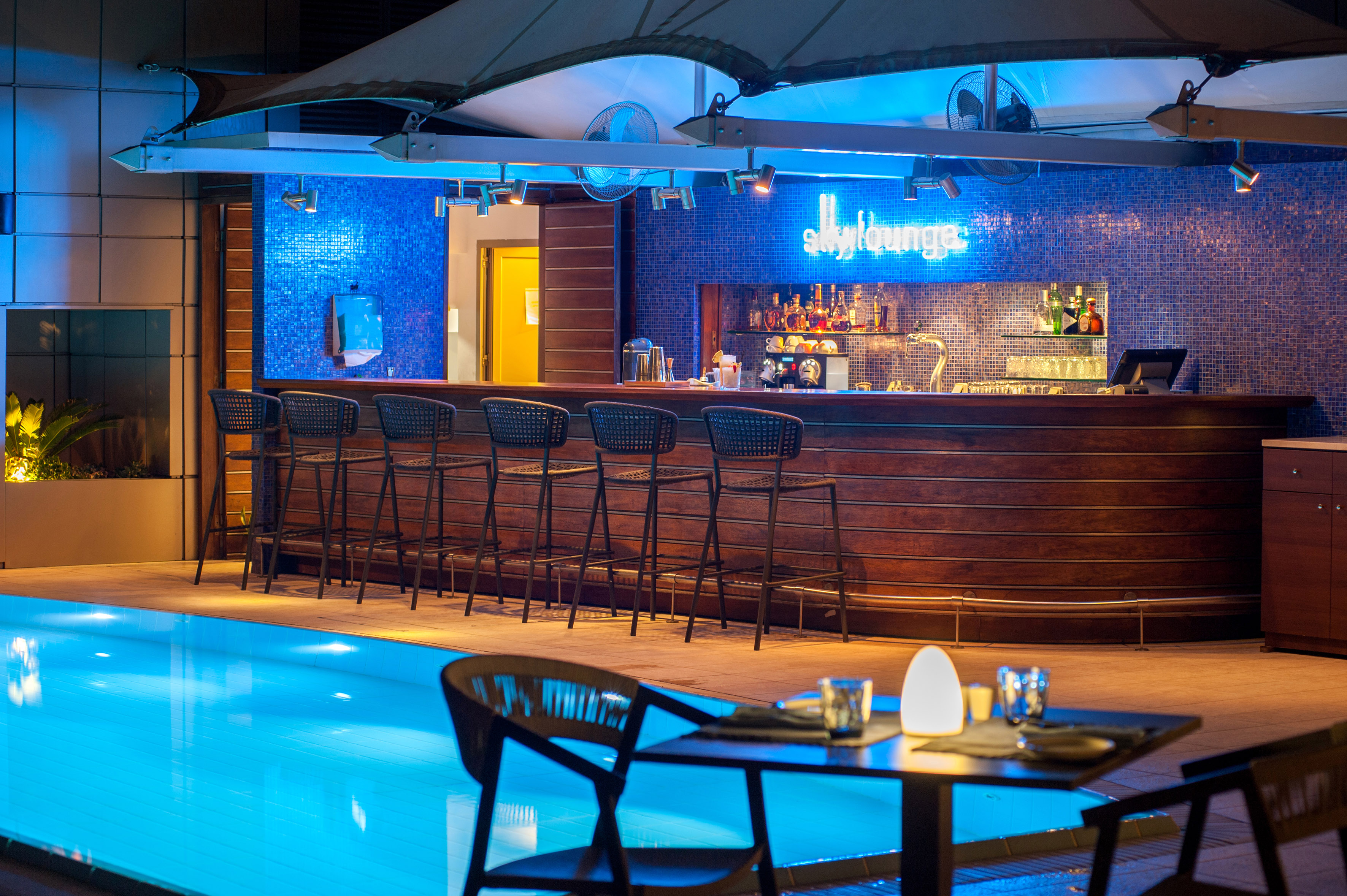 SkyLounge outdoor pool bar at night with blue neon and modern seating.