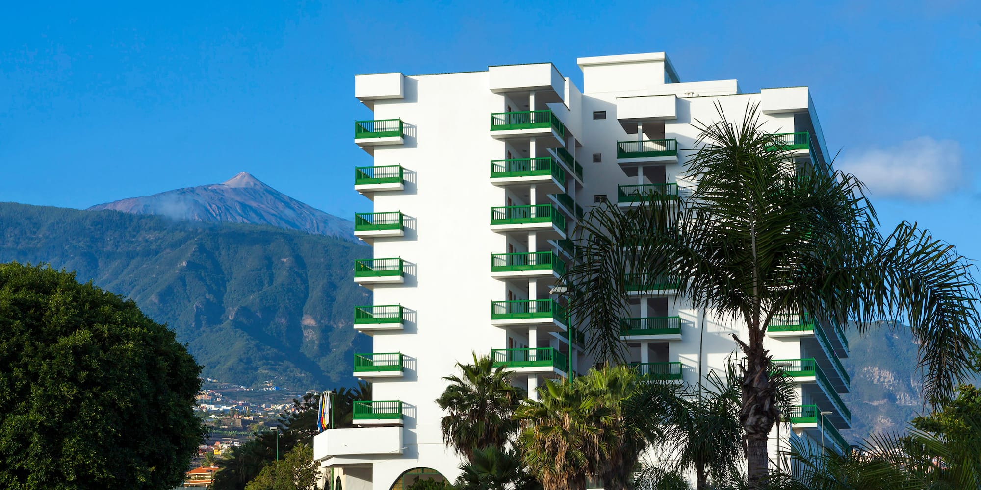 a white building with green balconies and trees
