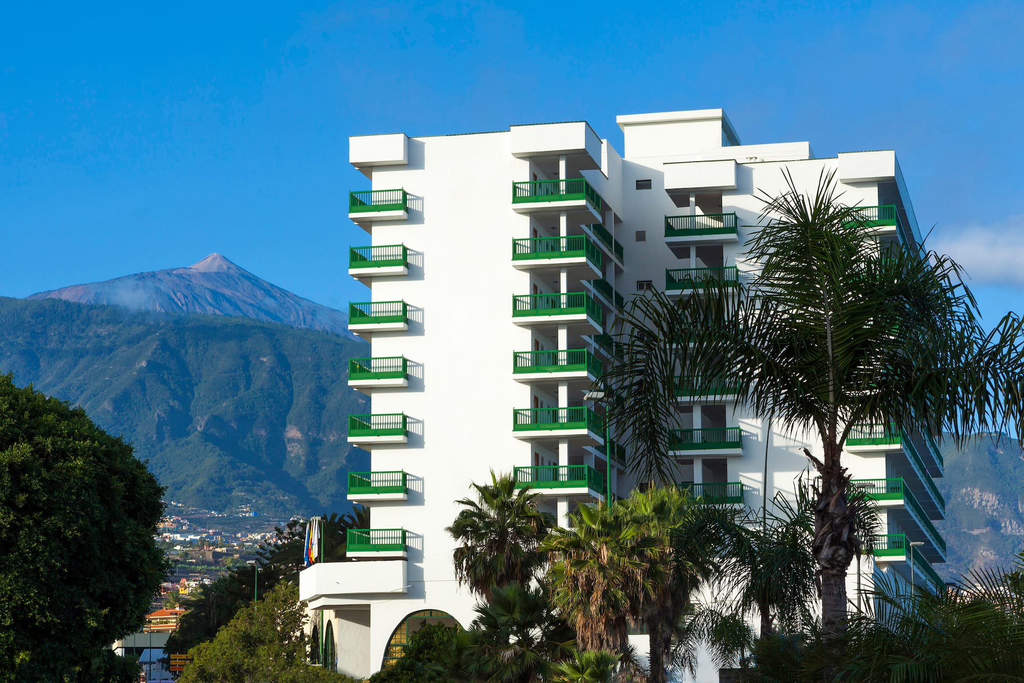 a white building with green balconies and trees