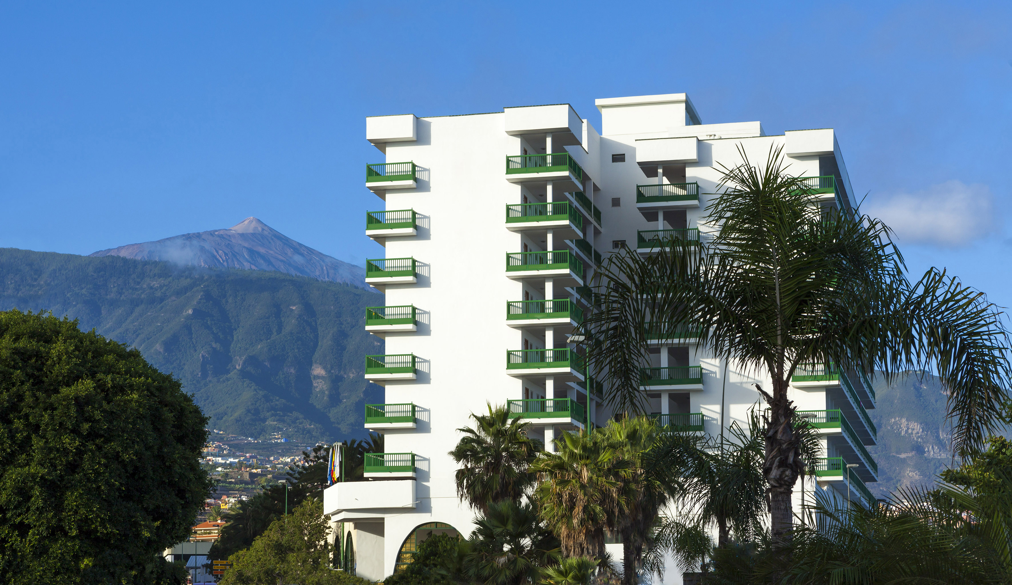 a white building with green balconies and trees