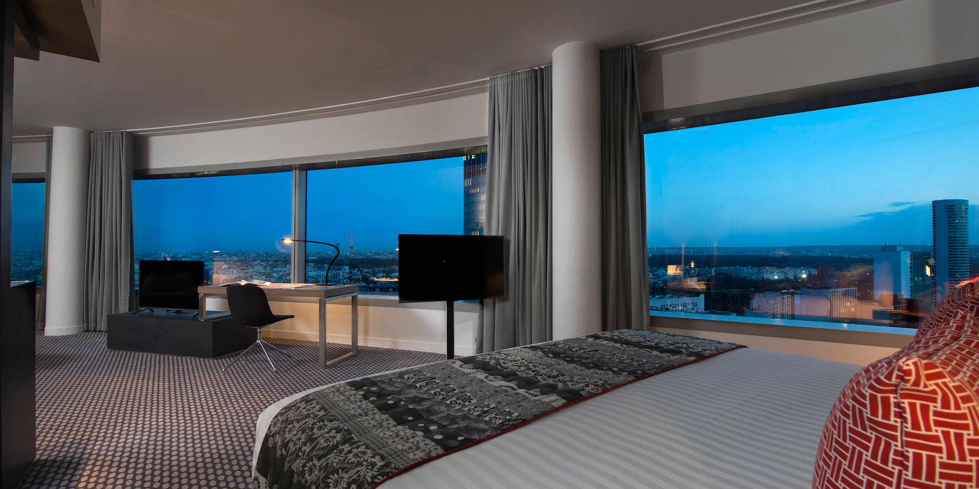 a room with a large bed and a desk and a large window