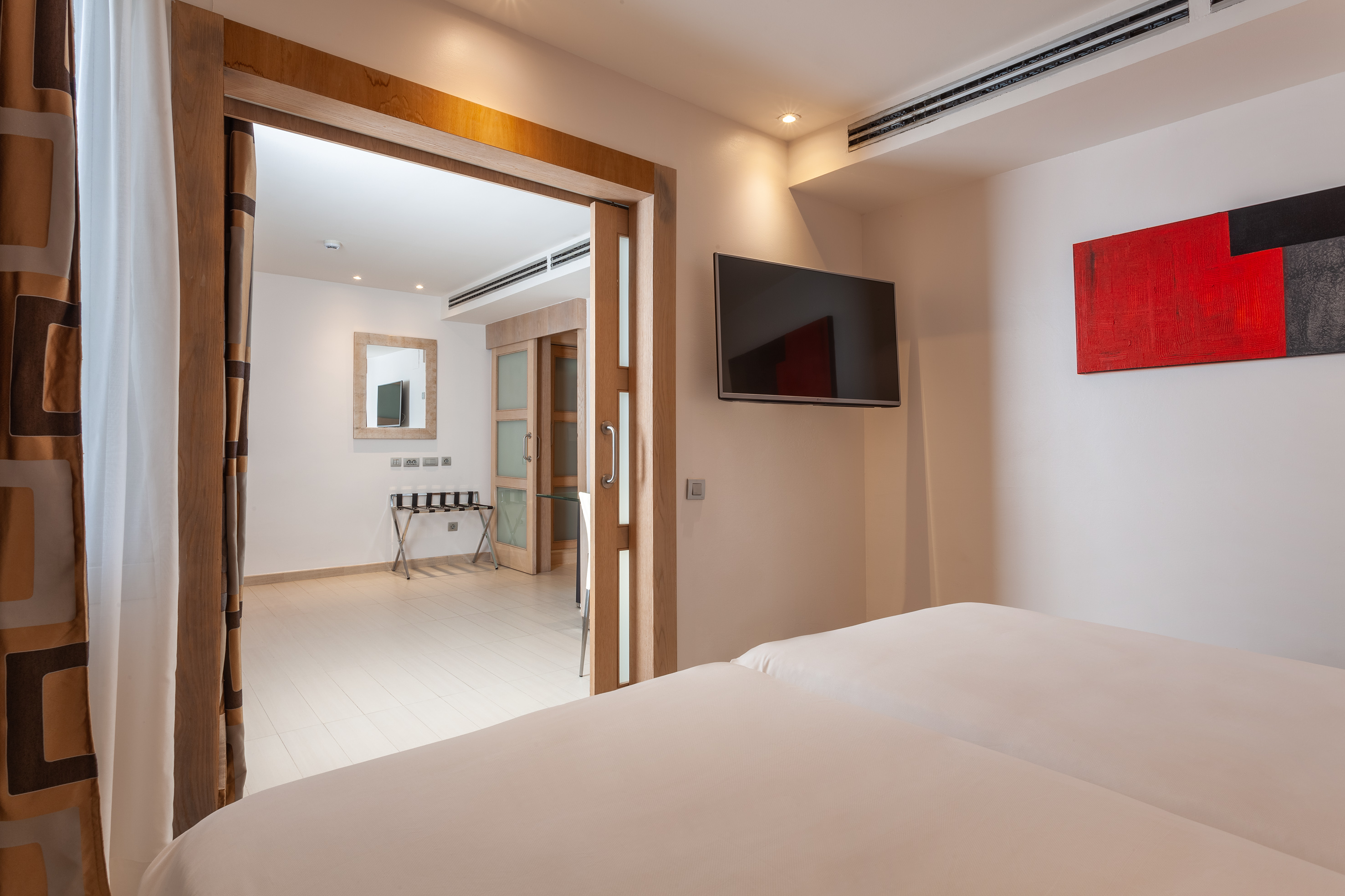 Modern hotel bedroom with white bed, TV, red art, and wooden sliding doors.